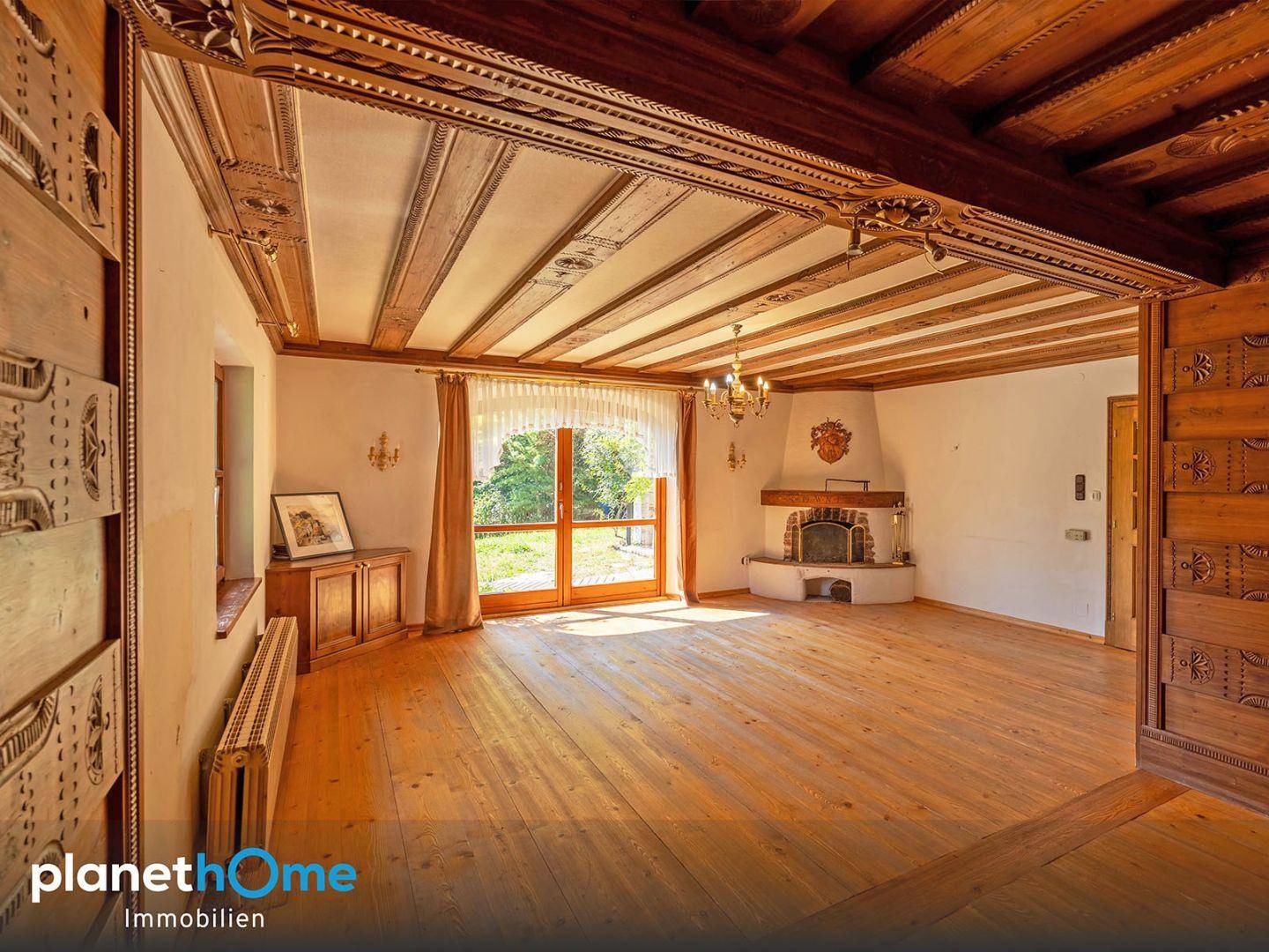 Geräumiges Wohnzimmer mit kunstvoll geschnitzter Holzdecke, Kamin und Holzboden, hell und einladend.