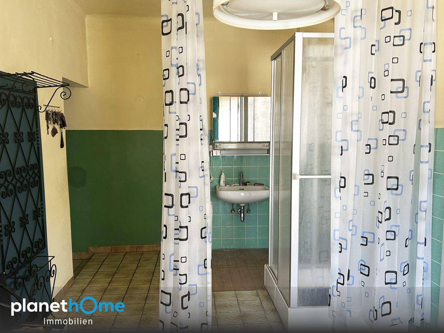 Badezimmer mit Duschkabine, Waschbecken und älteren Fliesen im Stil der 80er Jahre.
