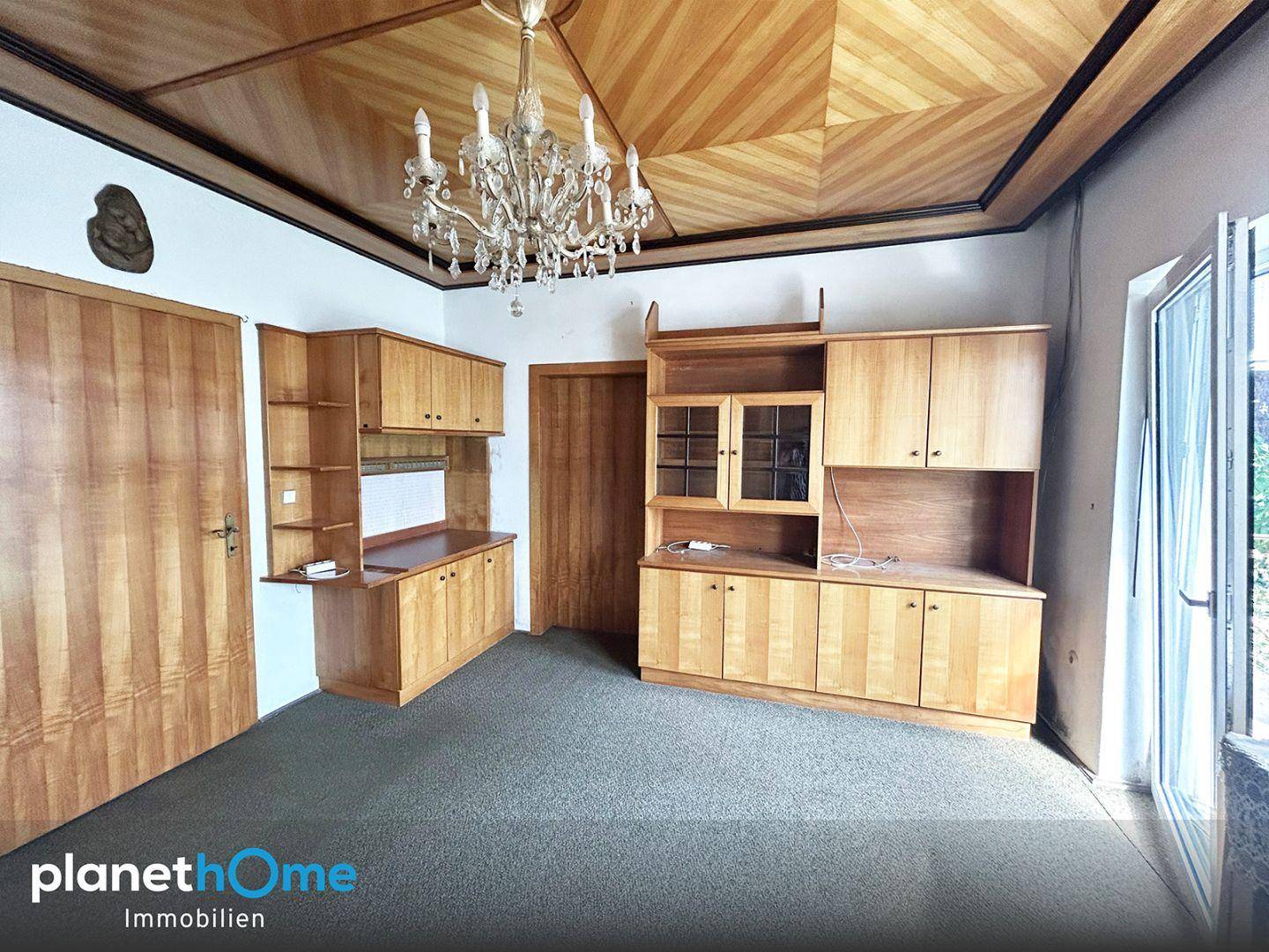 Wohnzimmer mit Holztäfelung an der Decke, Kronleuchter und Holzschränken im Landhausstil.
