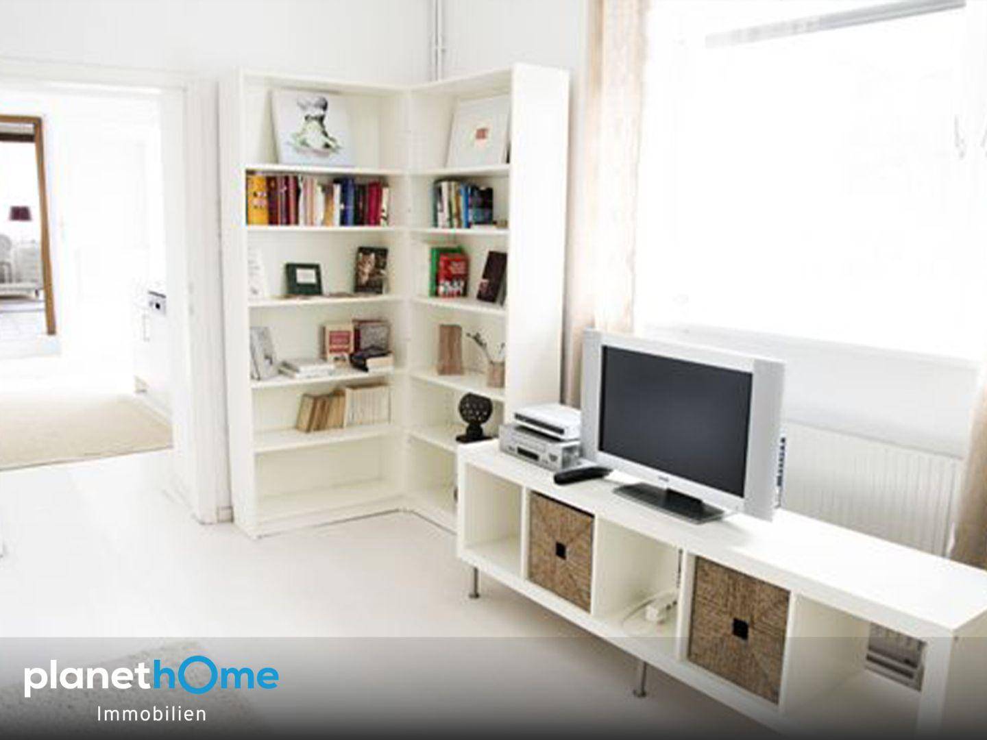 Heller Wohnbereich mit weißem Bücherregal, TV-Möbel und viel Tageslicht.