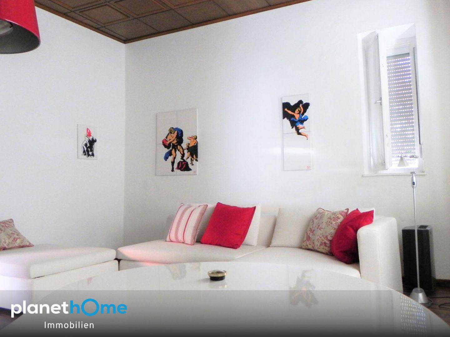Gemütliches Wohnzimmer mit weißem Sofa, roten Kissen und einer Holzdecke.