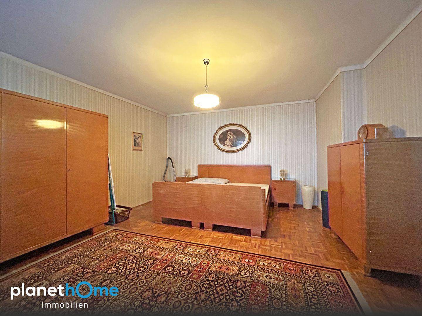 Schlafzimmer mit Holzparkett, Doppelbett, Kleiderschränken und einem gemusterten Teppich.