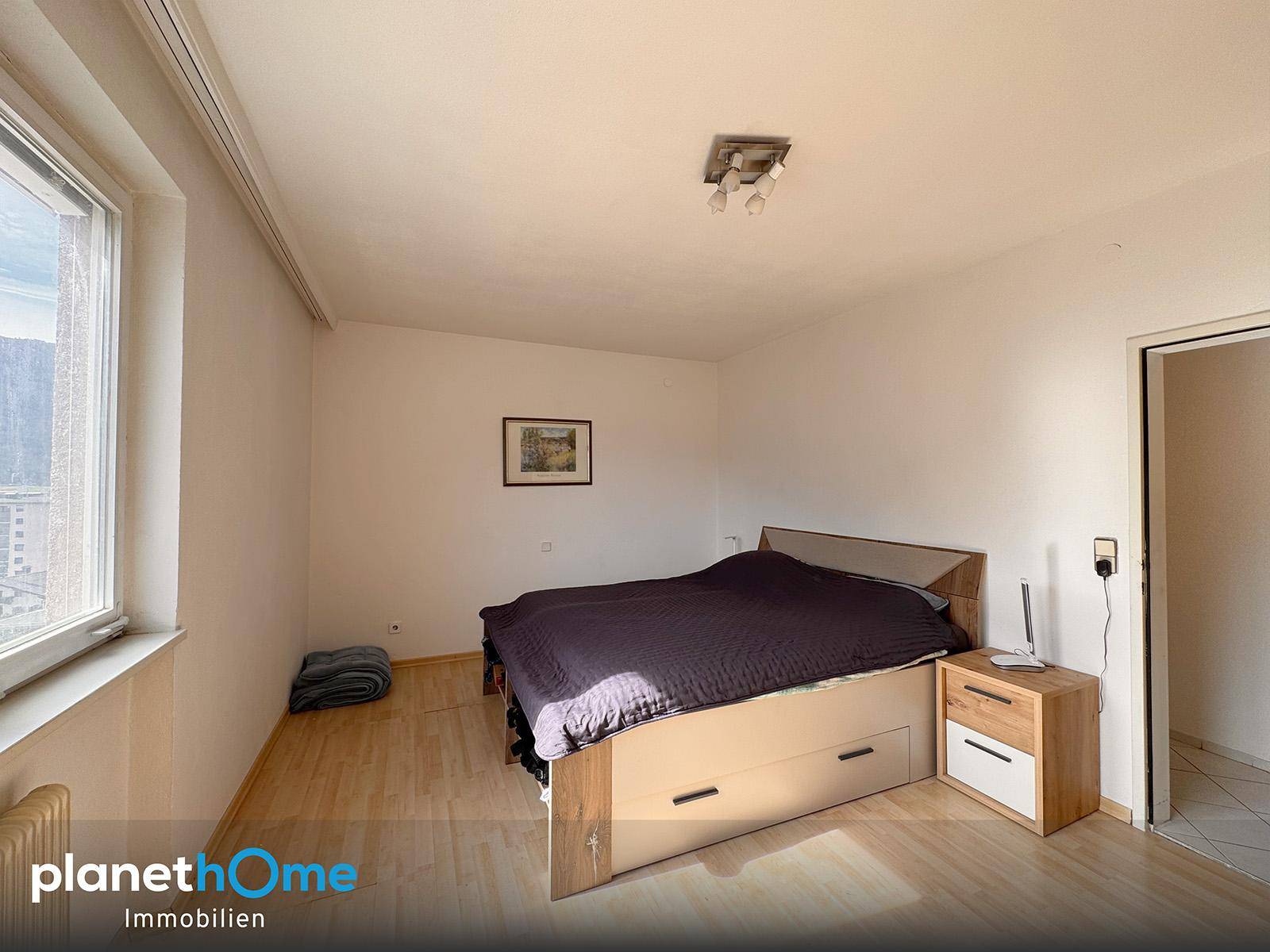 Schlafzimmer mit Laminatboden, Bett mit Stauraum und Fenster für natürliches Licht.