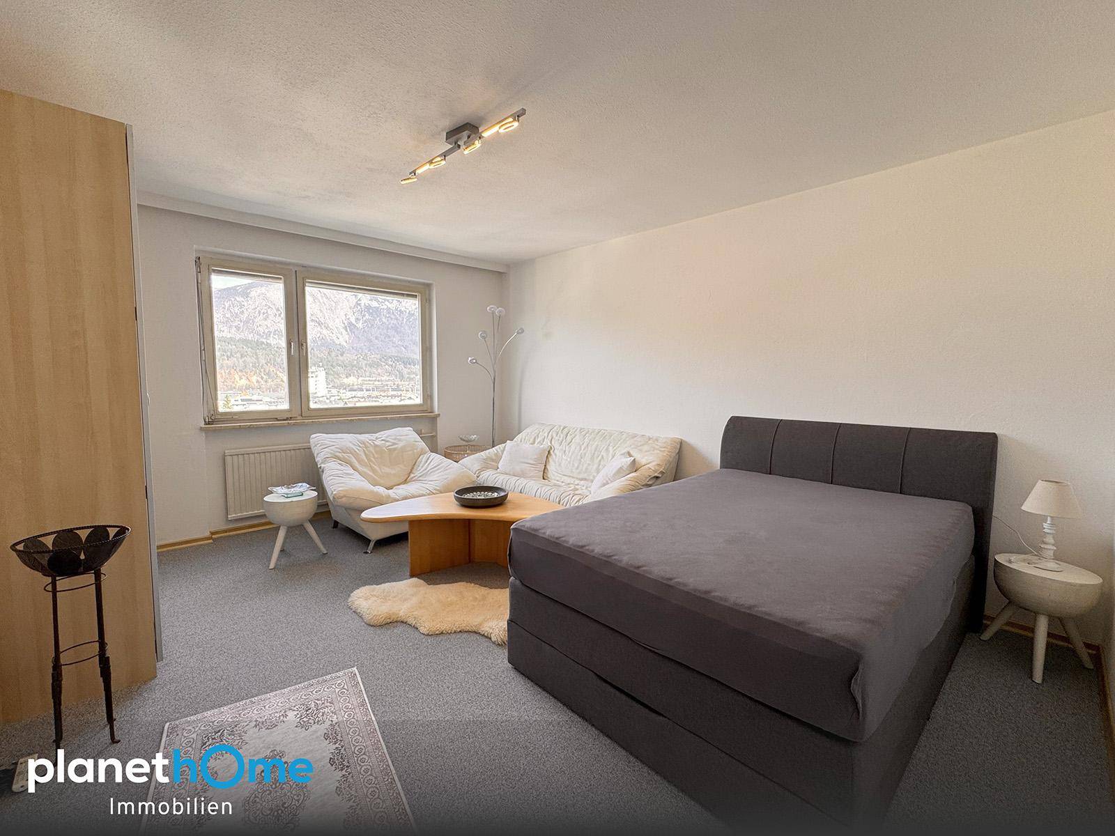 Gemütliches Schlafzimmer mit Teppichboden, Bett, Sofa und Fenster mit Bergblick.