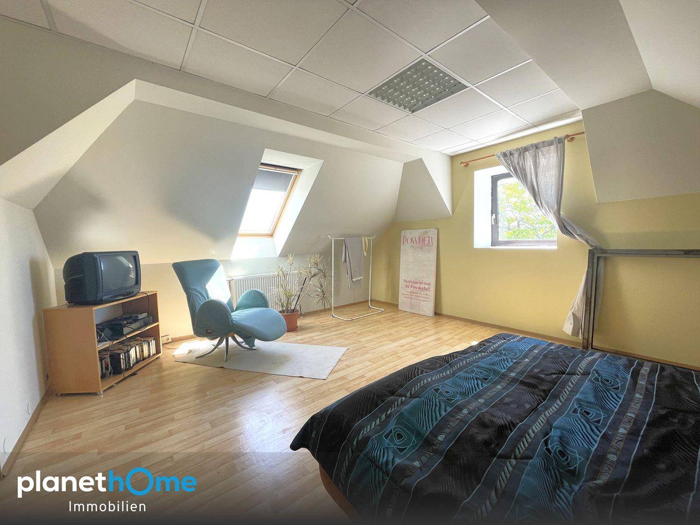 Helles Schlafzimmer im Dachgeschoss mit Dachschrägen, Holzboden und einem Dachfenster.