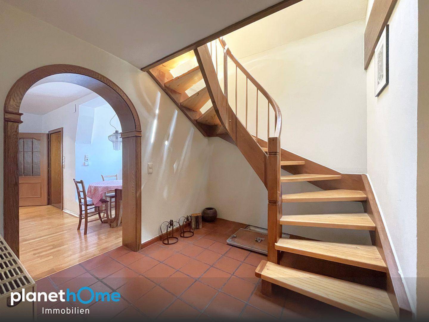 Eingangsbereich mit rustikaler Holztreppe und Terrakottafliesen, führt zu einem Essbereich.