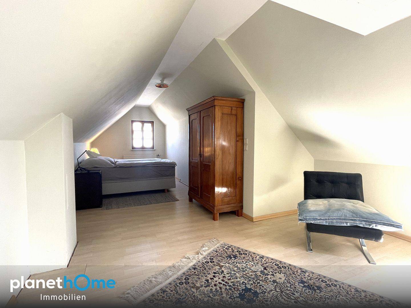 Schlafzimmer im Dachgeschoss mit Dachschrägen, Holzboden und einem traditionellen Kleiderschrank.