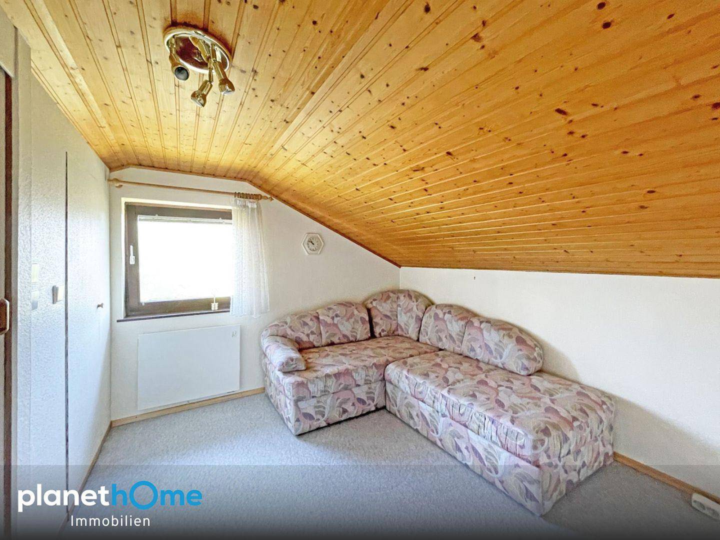 Dachgeschosszimmer mit gemütlicher Eckcouch, Holzdecke und Fenster mit Blick ins Grüne.