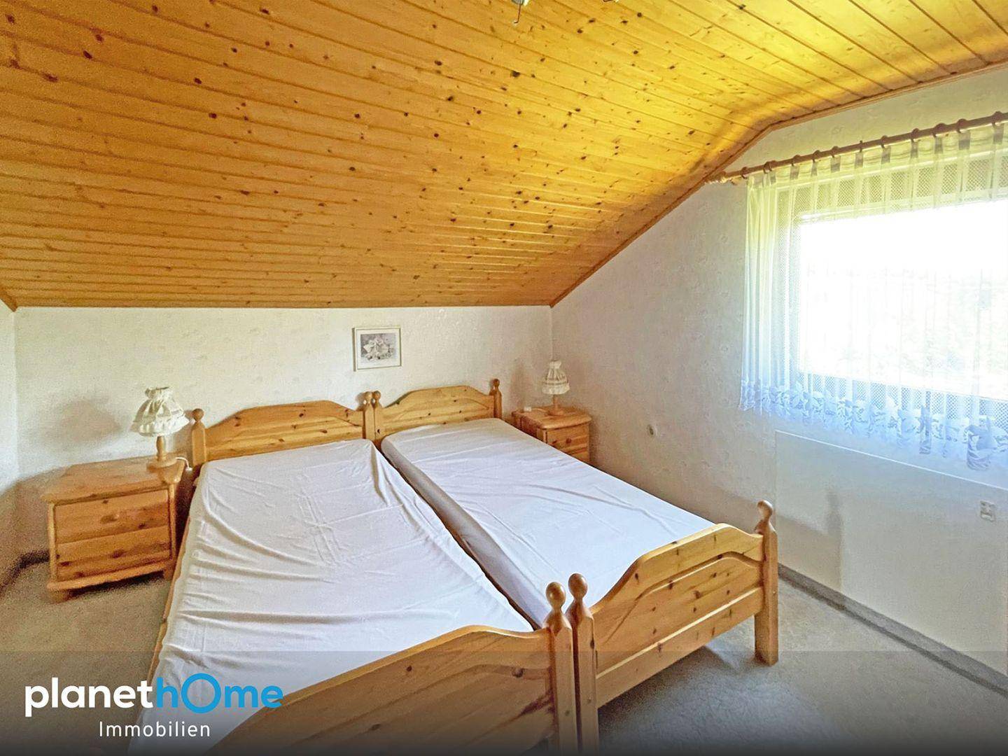 Schlafzimmer im Dachgeschoss mit Holzverkleidung, zwei Einzelbetten und schrägen Decken.