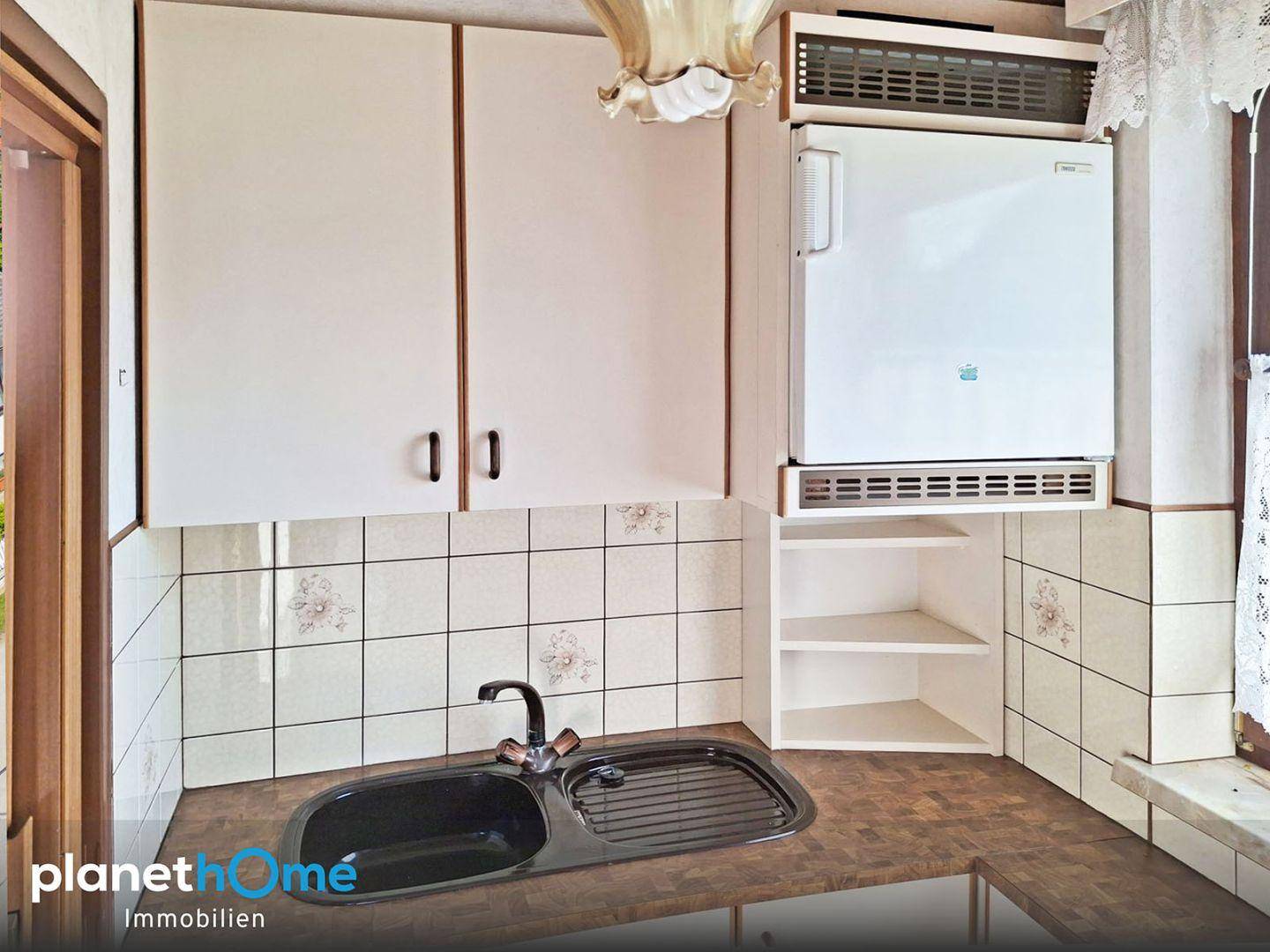 Kleine Küche mit weißen Schränken, Spüle und integriertem Kühlschrank im Landhausstil.