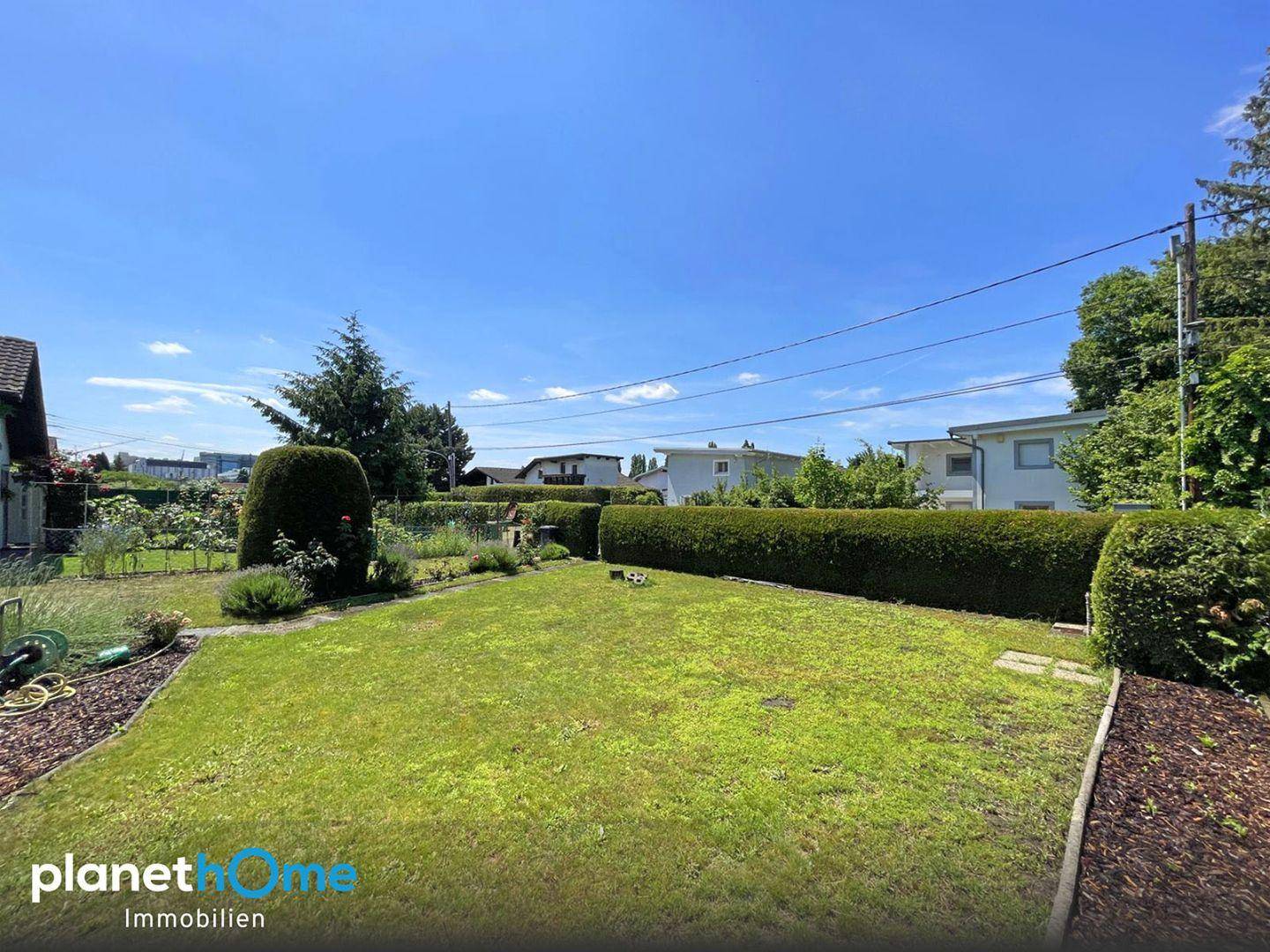 Weitläufiger Gartenbereich mit gepflegtem Rasen und hohen Hecken unter klarem blauem Himmel.