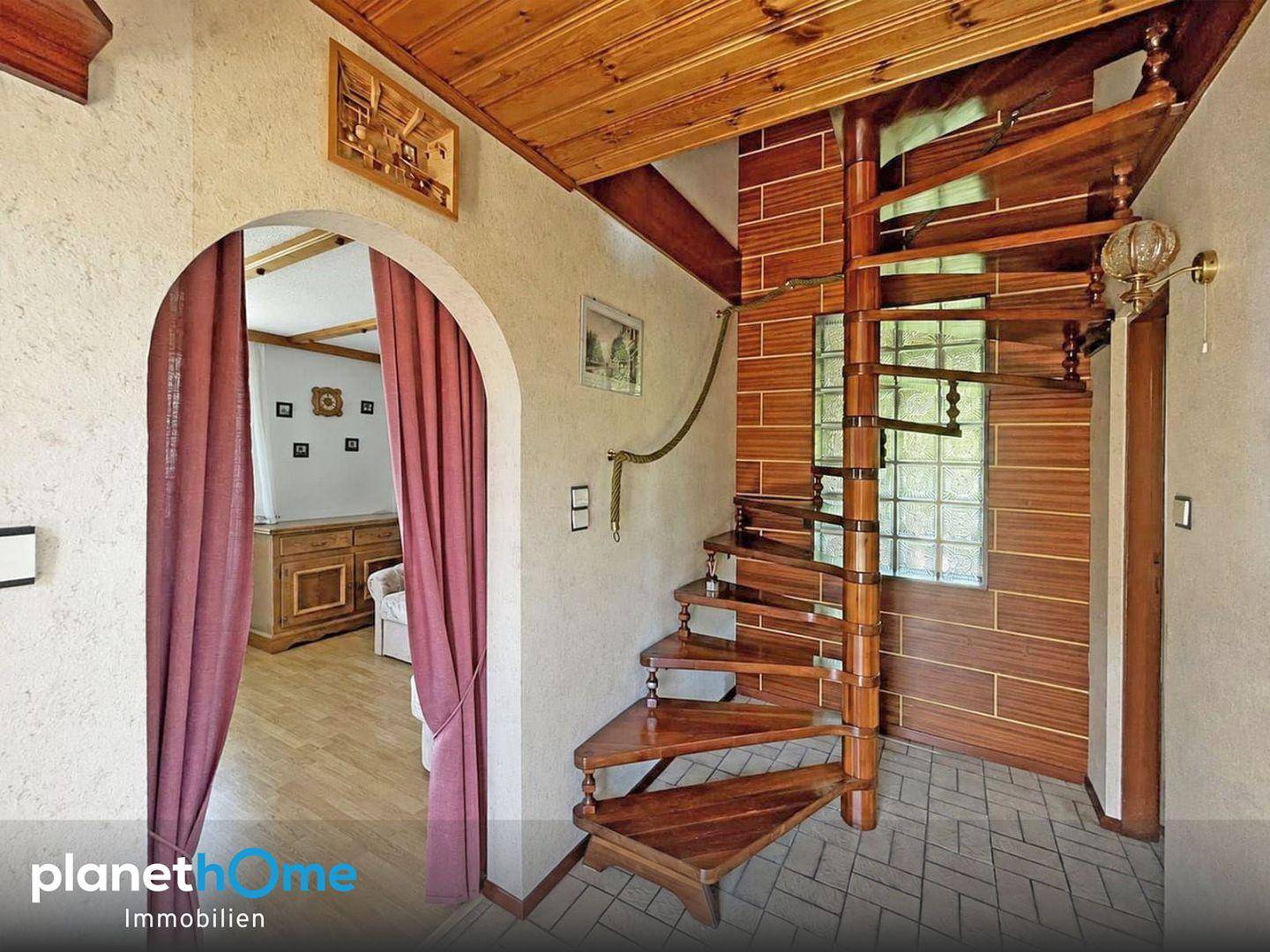 Eingangsbereich mit Holzwendeltreppe, gefliestem Boden und Zugang zu weiteren Räumen.