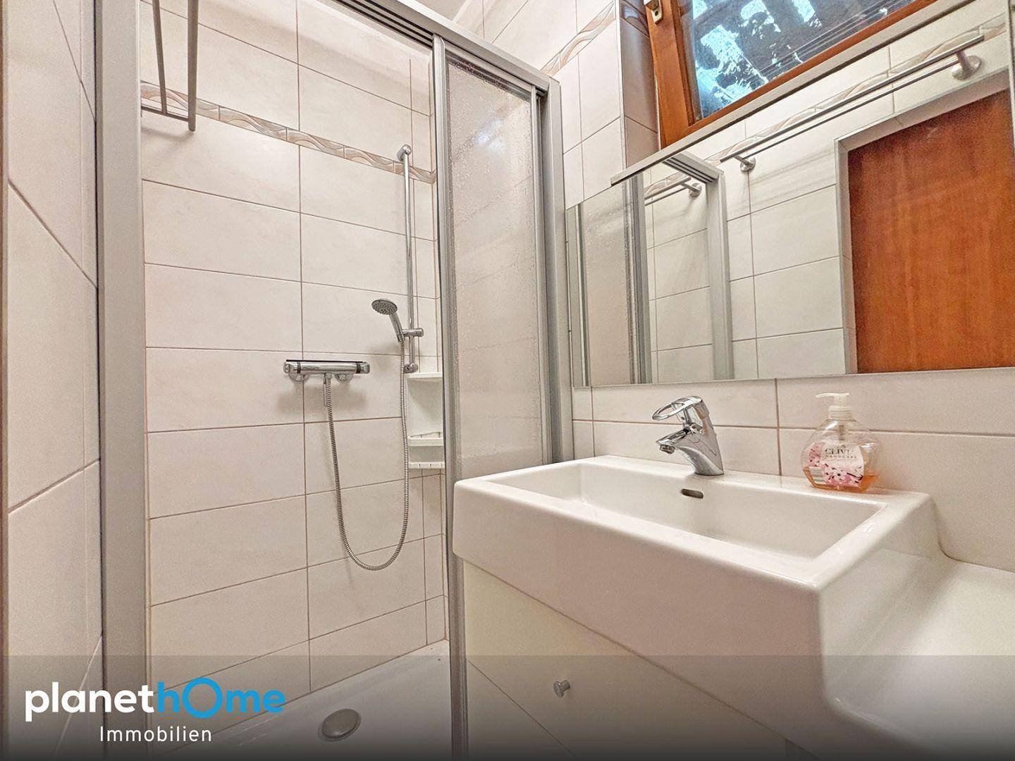 Gefliestes Badezimmer mit Duschkabine, Einzelwaschbecken und Fenster.