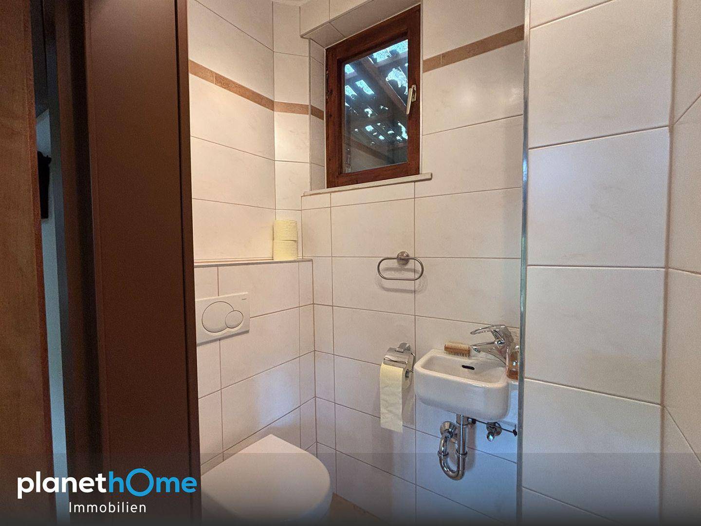 Kleines Gäste-WC mit wandhängendem WC, Handwaschbecken und Fenster.