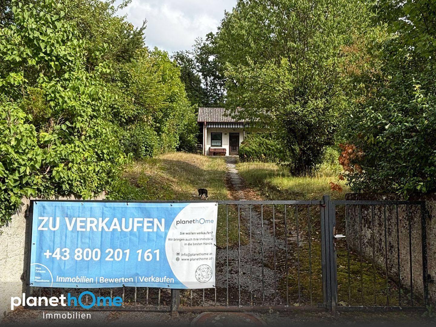 Einfahrt zum Grundstück mit 'Zu Verkaufen'-Schild und Blick auf das Haus.