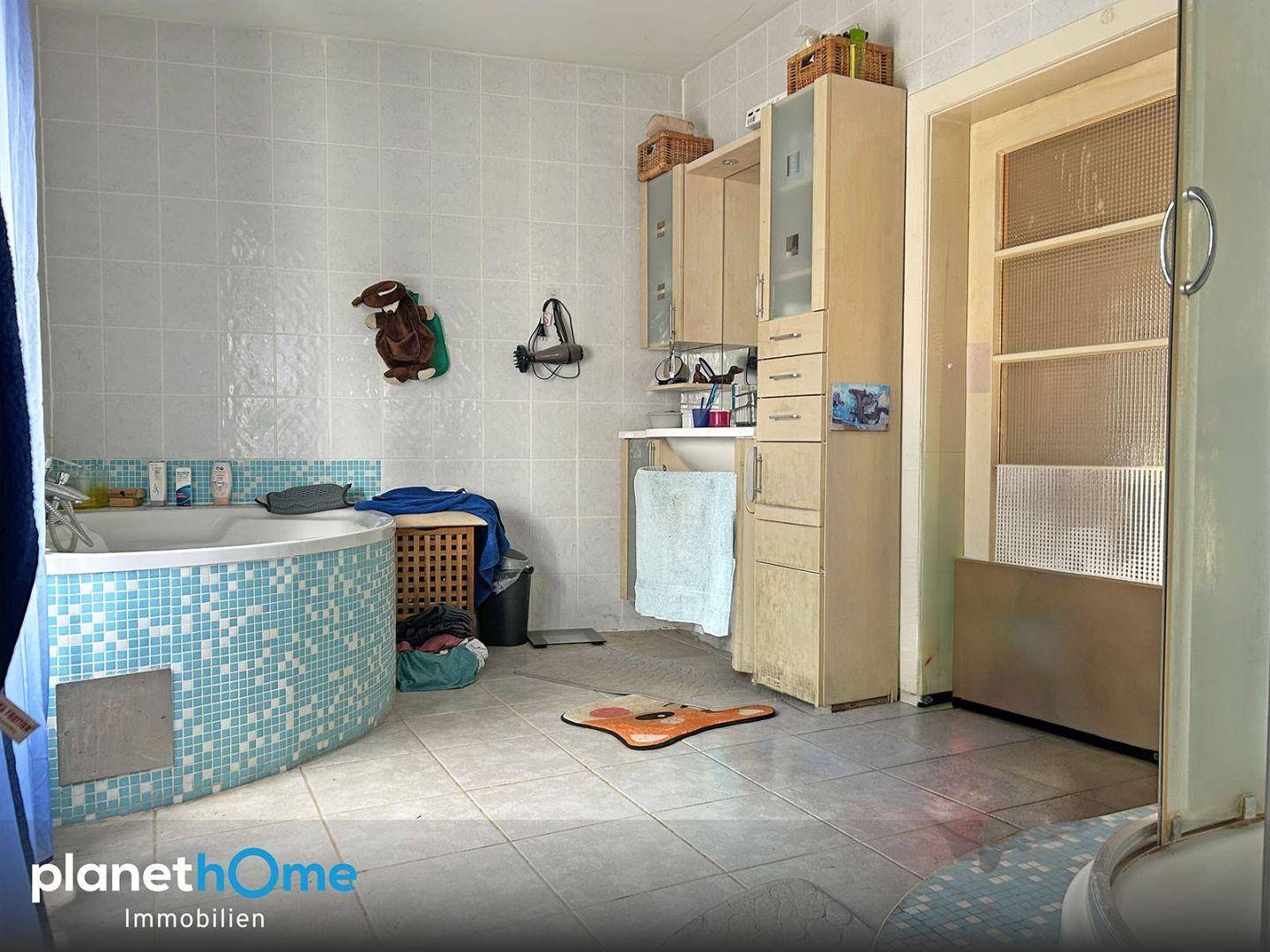 Badezimmer mit Eckbadewanne, blauen Mosaikfliesen und hellen Wandfliesen.