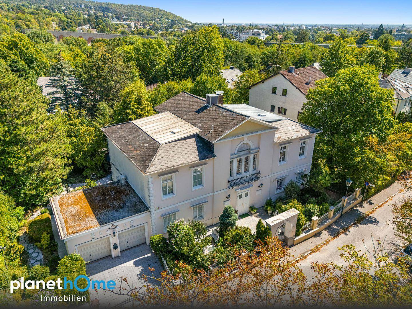 Luftaufnahme der Villa mit umliegendem Grün und Blick auf die Stadt im Hintergrund.