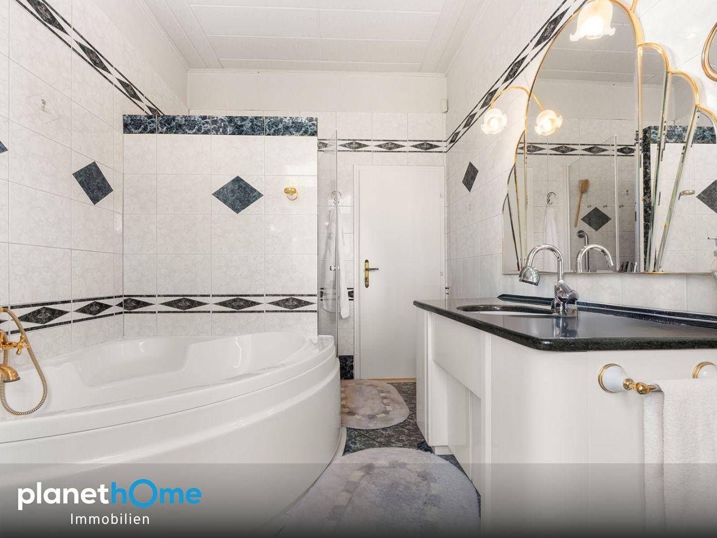 Badezimmer mit Eckbadewanne, Doppelwaschbecken und Fliesen in Schwarz-Weiß.