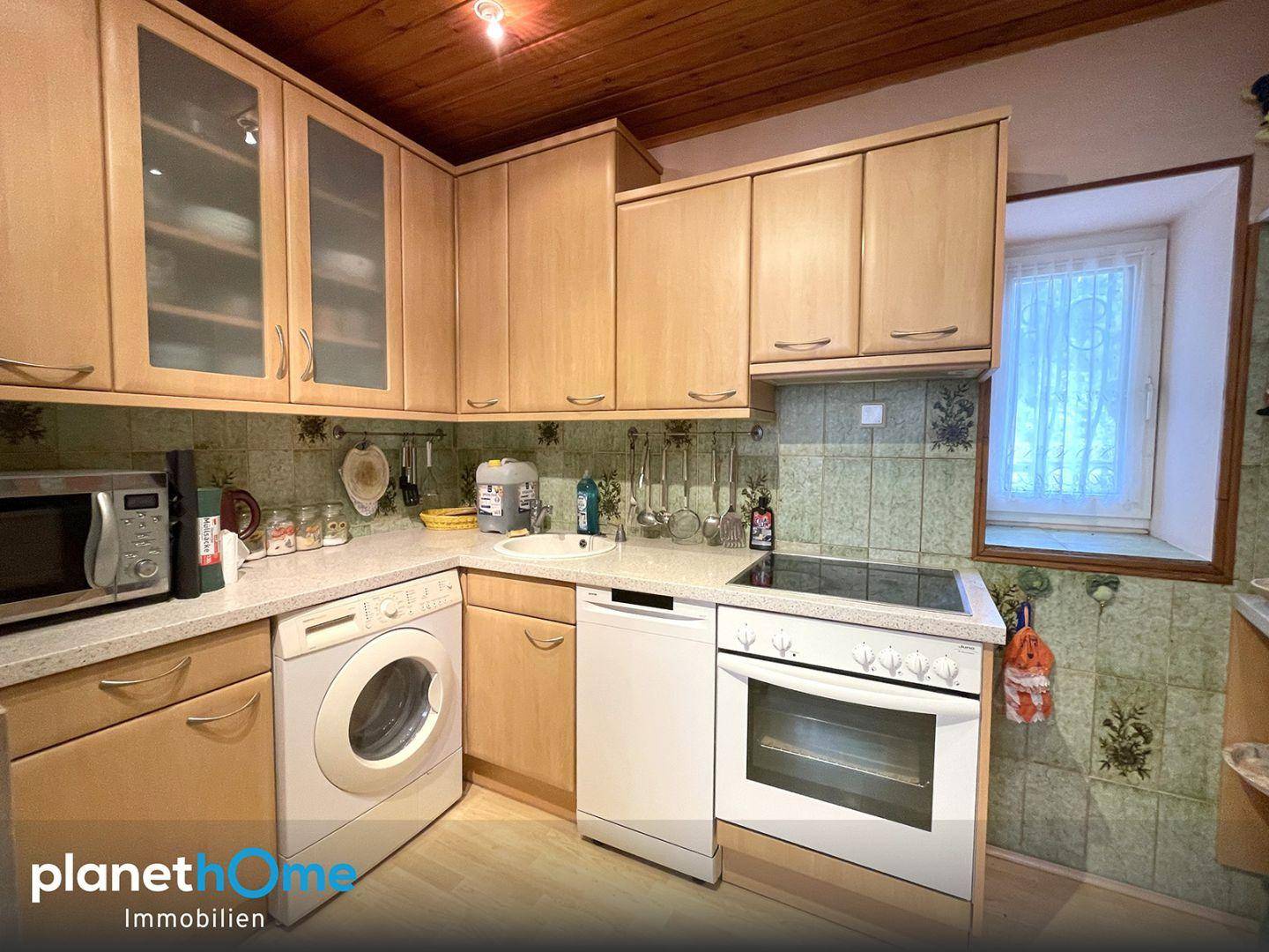 Kleine Küche mit Holzschränken, Fliesenrückwand und integrierten Haushaltsgeräten sowie Fenster.
