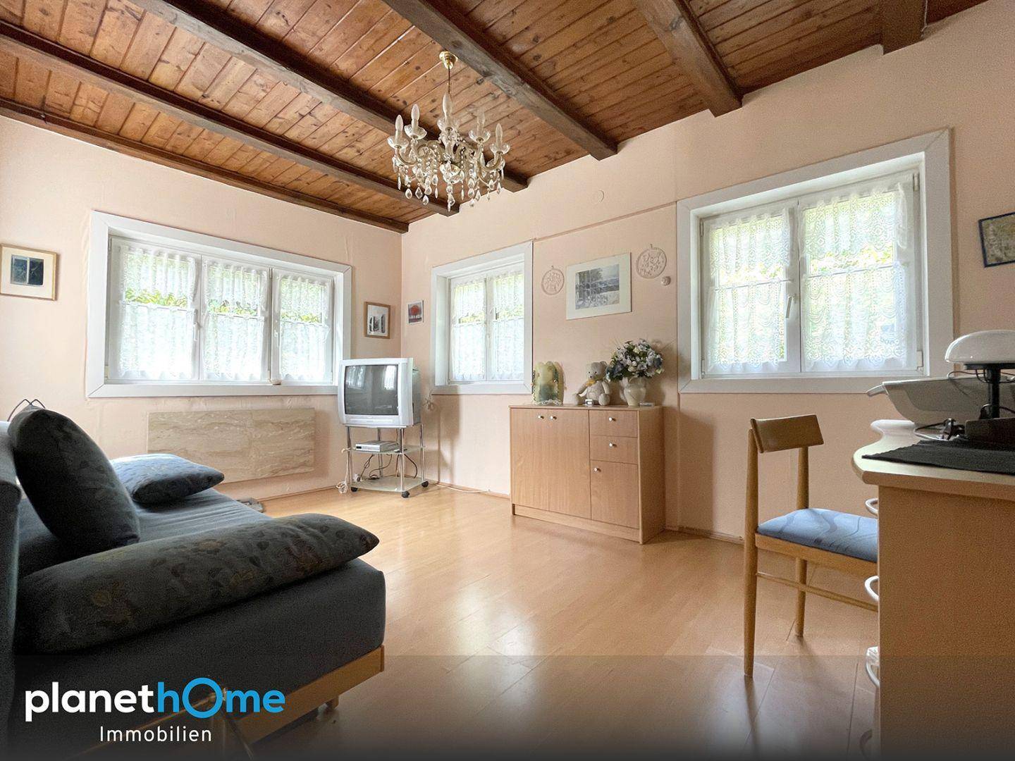 Helles Wohnzimmer mit Holzbalkendecke, Parkettboden und mehreren Fenstern für viel Tageslicht.