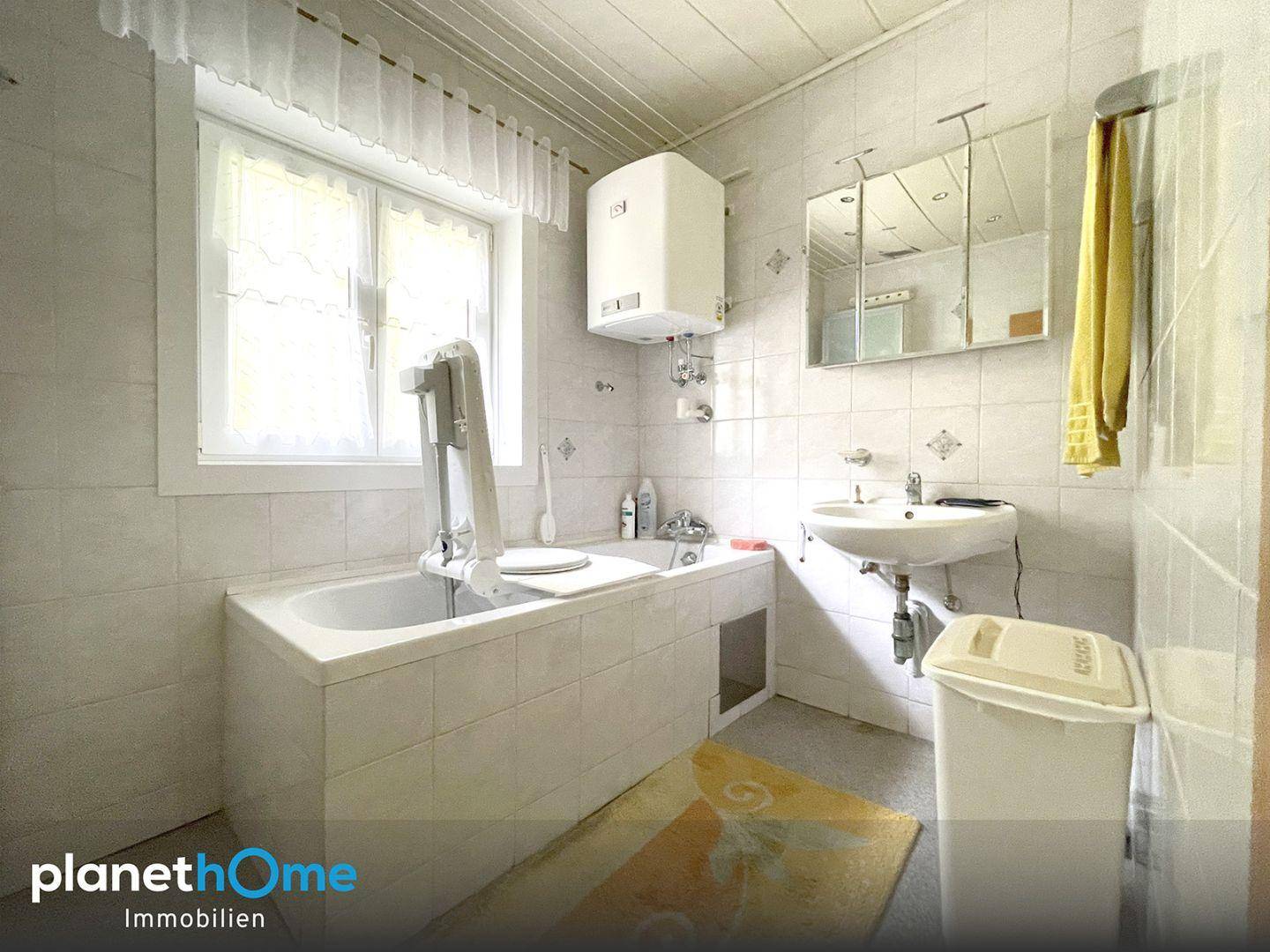 Badezimmer mit weißen Fliesen, Badewanne, Waschbecken und Fenster für natürliches Licht.