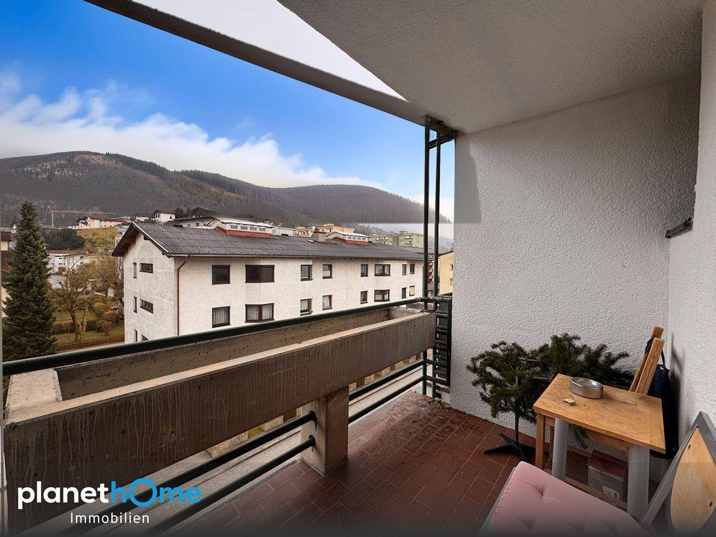 Balkon mit Blick auf die umliegenden Gebäude und die bewaldeten Hügel.