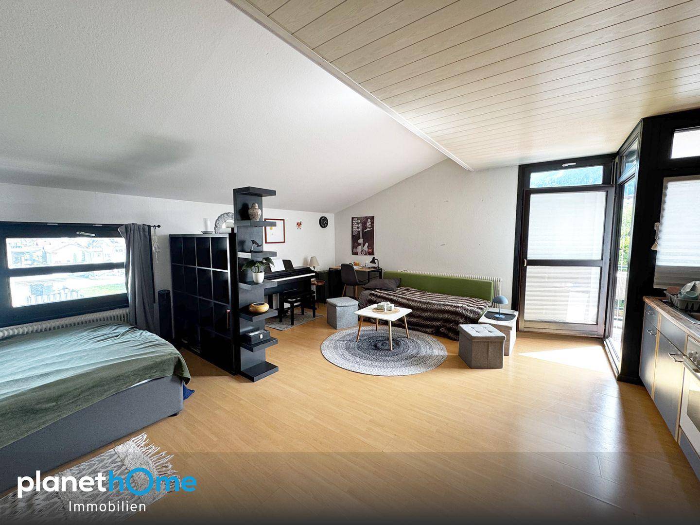 Heller offener Wohnbereich mit integrierter Küche, Schlafbereich und Zugang zum Balkon.