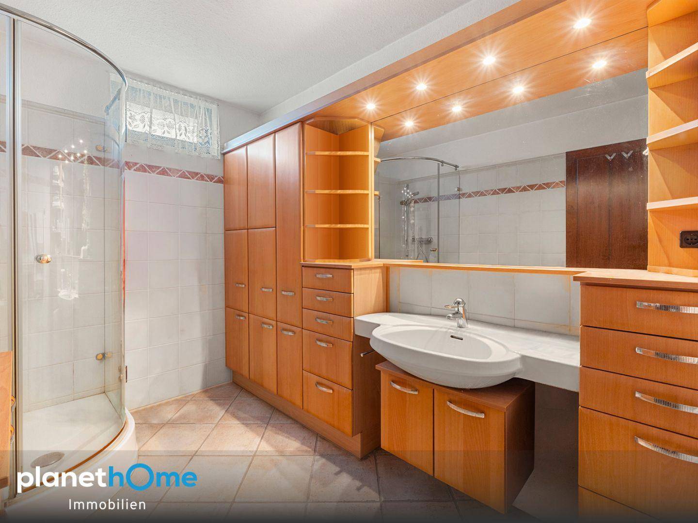 Badezimmer mit Duschkabine, Einzelwaschbecken, großem Spiegel und praktischen Holzschränken.