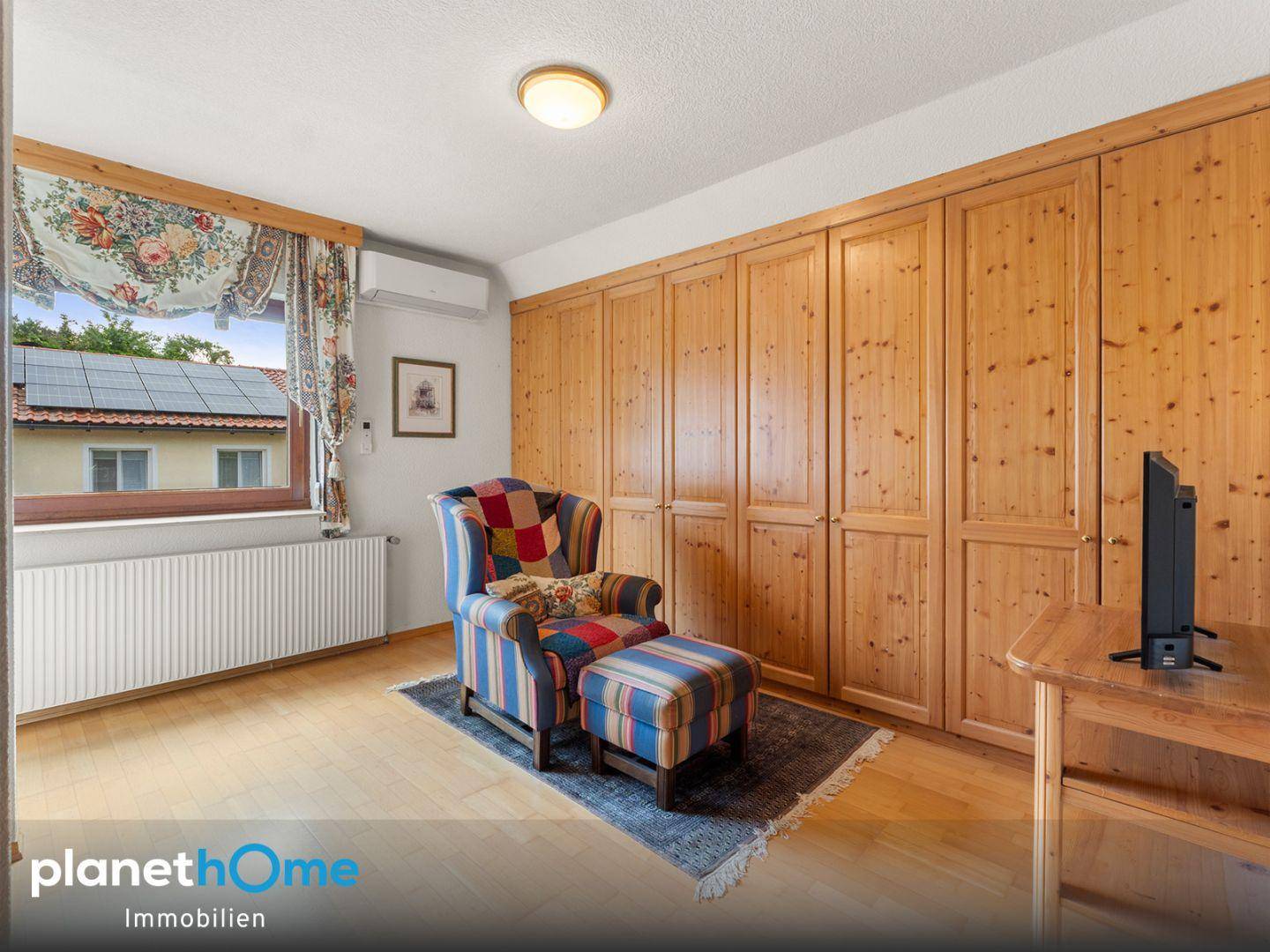 Schlafzimmer mit maßgefertigten Holzschränken, einem bequemen Sessel und Blick ins Grüne.