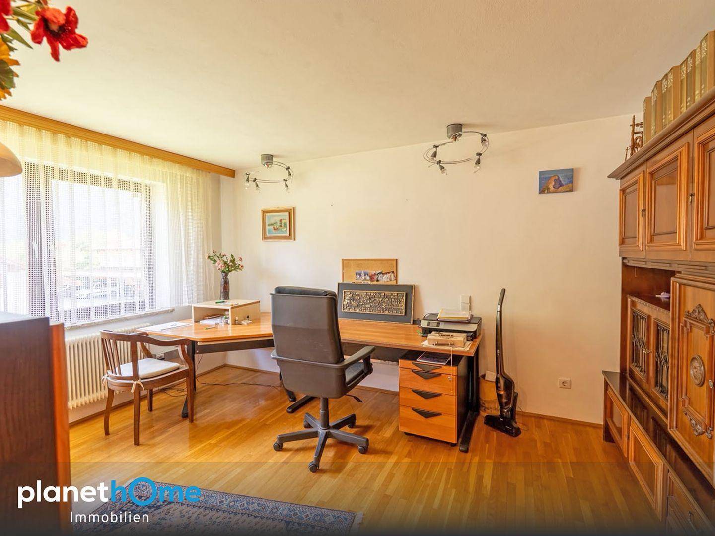 Geräumiges Arbeitszimmer mit Holzschreibtisch, Bürostuhl und großem Fenster für viel Tageslicht.