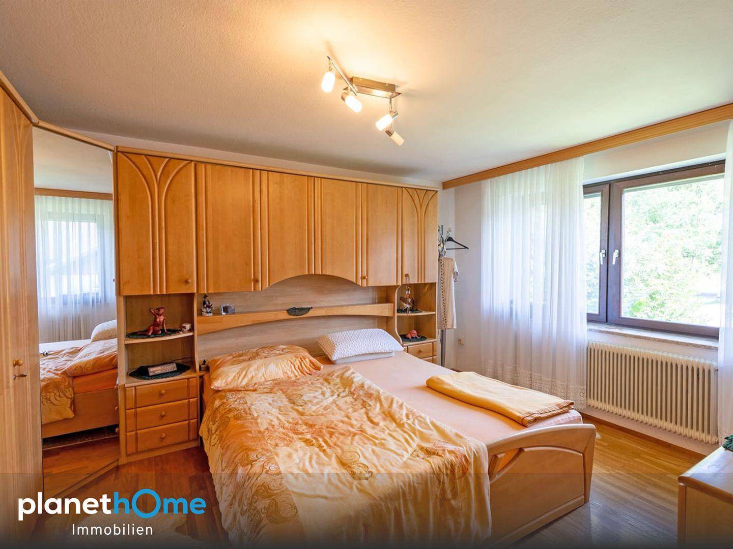 Helles Schlafzimmer mit Holzbett, Einbauschränken und großem Fenster mit Blick ins Grüne.
