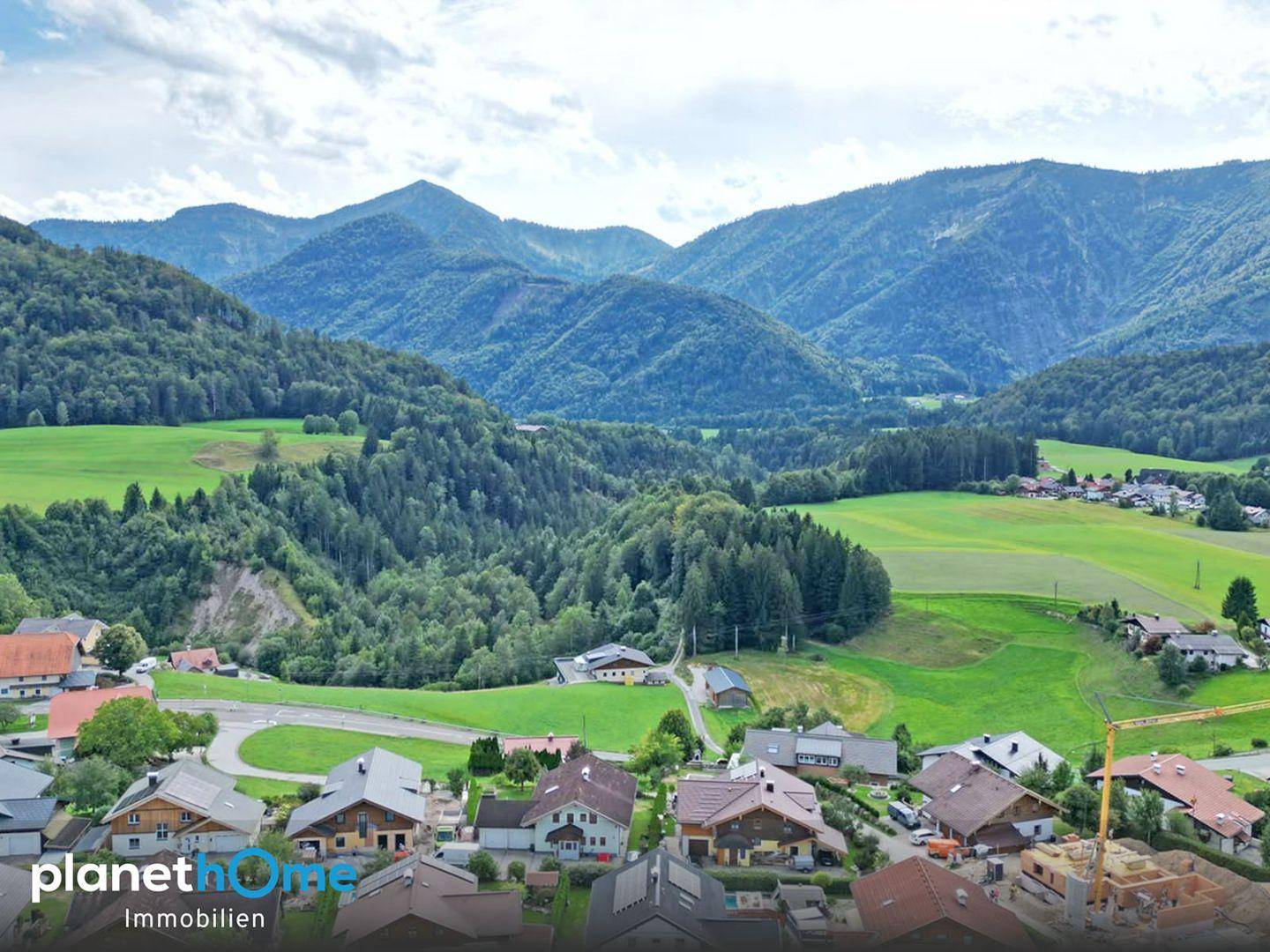 Panoramablick auf die umliegende Berglandschaft und das Tal mit verstreuten Häusern und viel Grün.