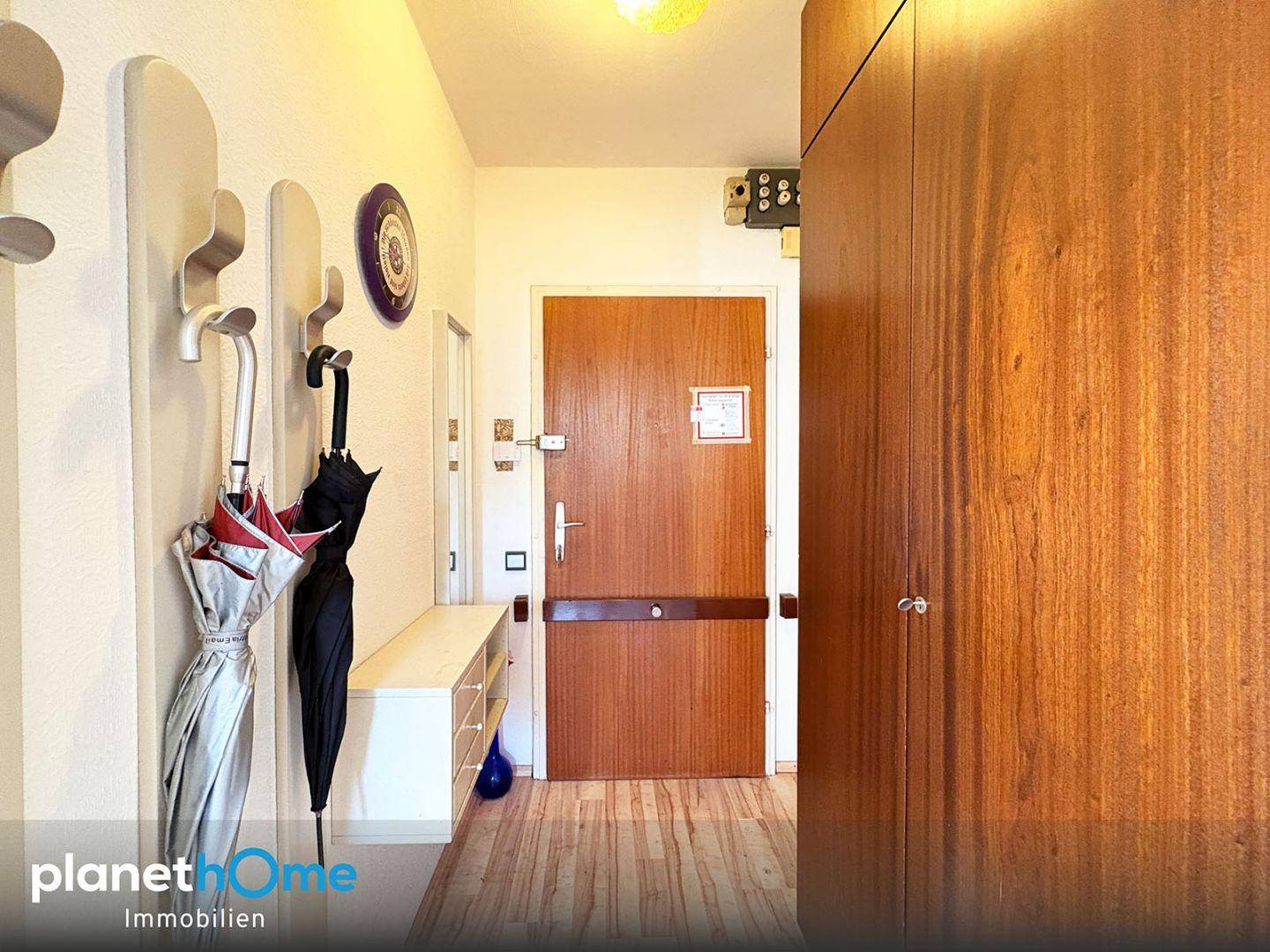 Eingangsbereich mit Garderobe, Schuhablage und einer Holztür, die in die Wohnung führt.