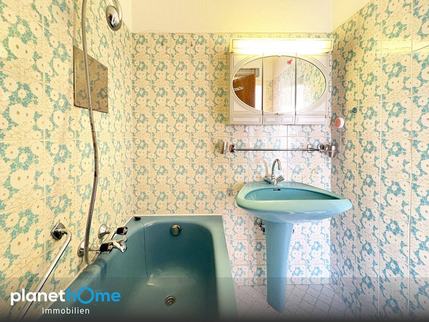 Badezimmer im 80er-Jahre-Stil mit blauer Badewanne, Waschbecken und gemusterten Wandfliesen.
