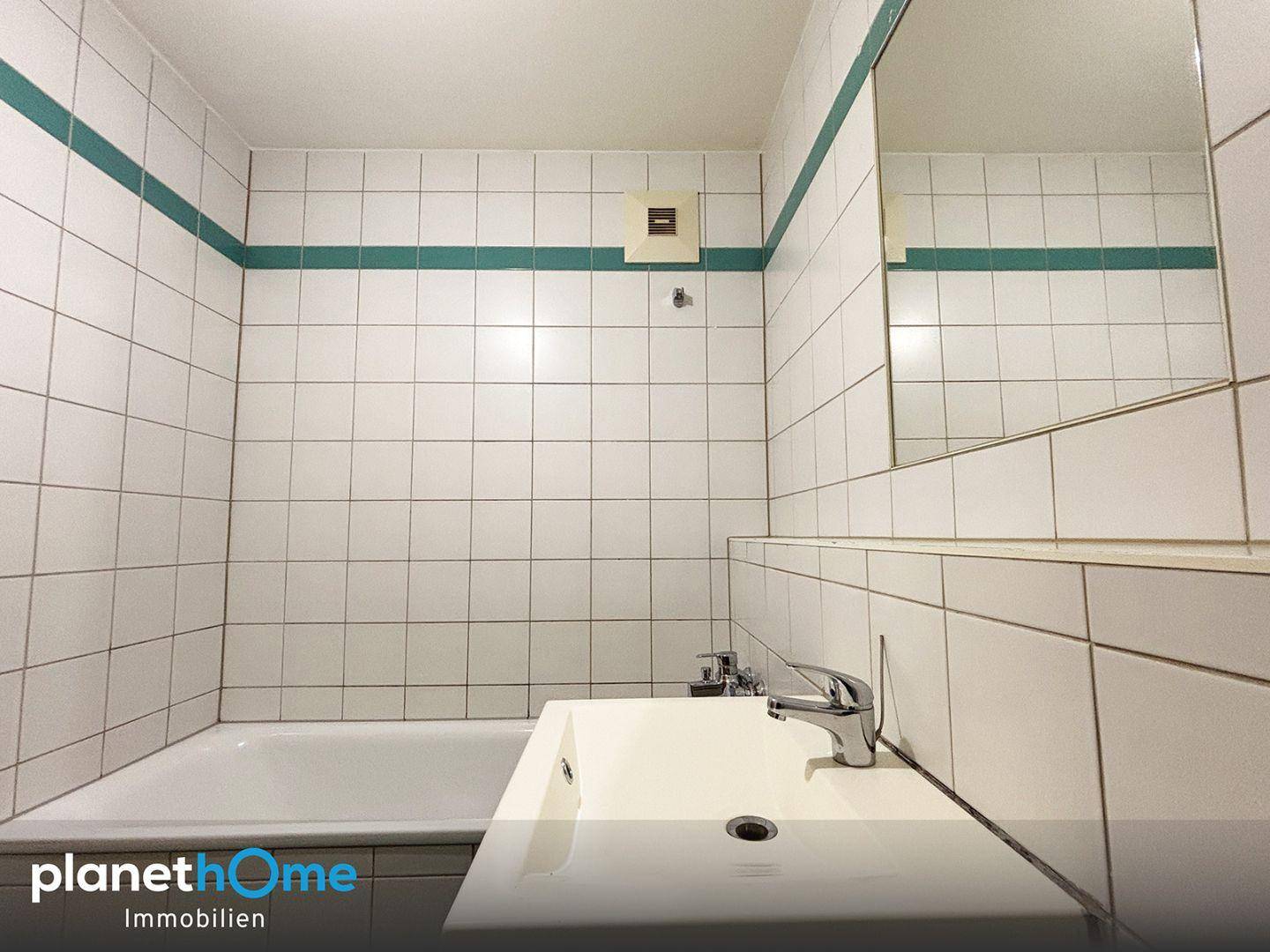 Badezimmer mit Badewanne, Waschtisch und weißen Fliesen mit grüner Dekorlinie.
