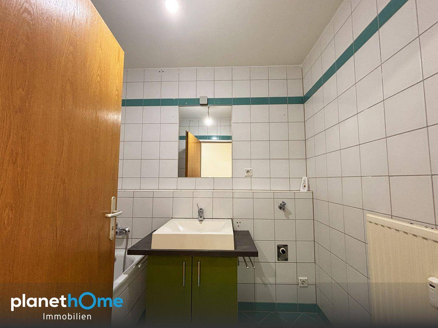 Badezimmer mit weißen Fliesen, grünen Akzenten, Waschtisch und integrierter Badewanne.