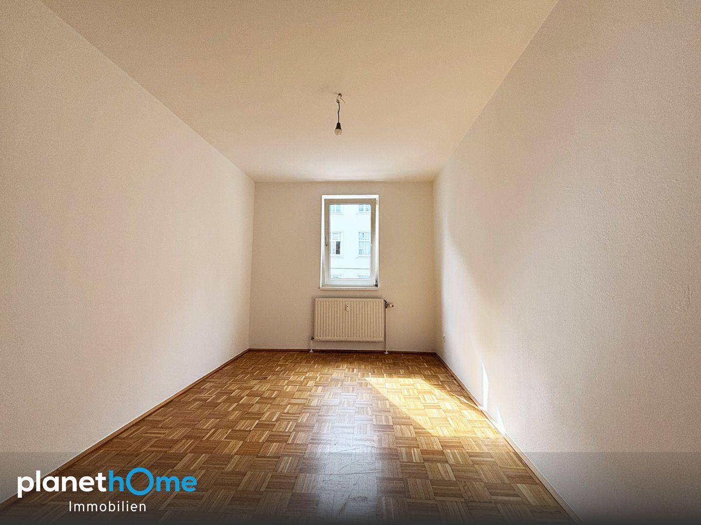 Gemütliches Zimmer mit Parkettboden, weiß gestrichenen Wänden und einem Fenster.
