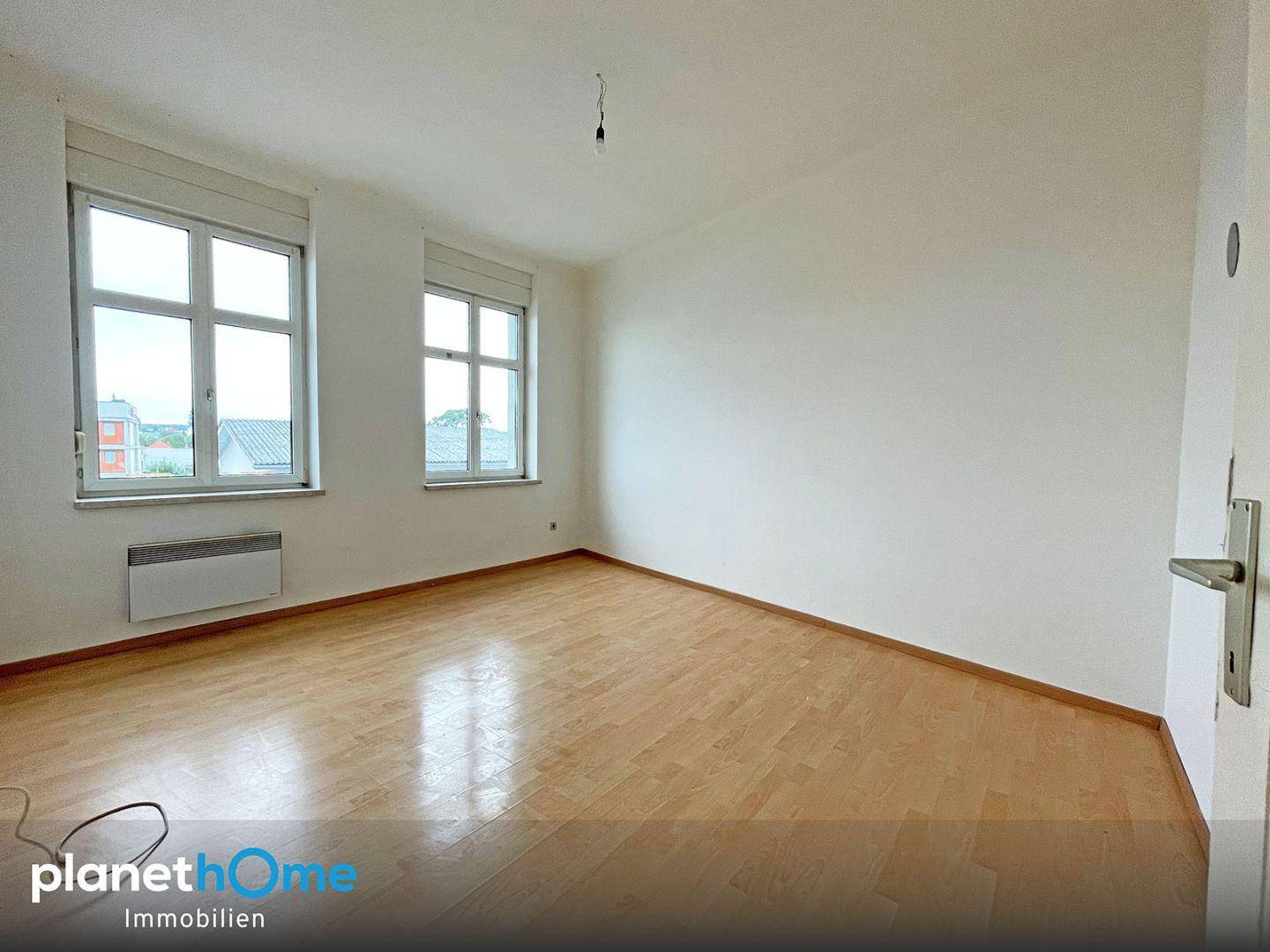 Geräumiges Zimmer mit hellem Parkettboden und großen Fenstern, ideal für Wohn- oder Schlafbereich.