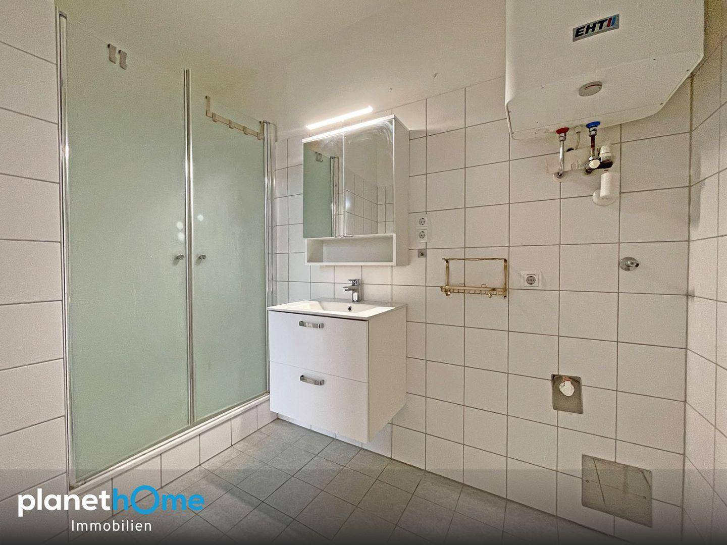 Gefliestes Badezimmer mit Duschkabine, modernem Waschbeckenunterschrank und praktischem Spiegelschrank.