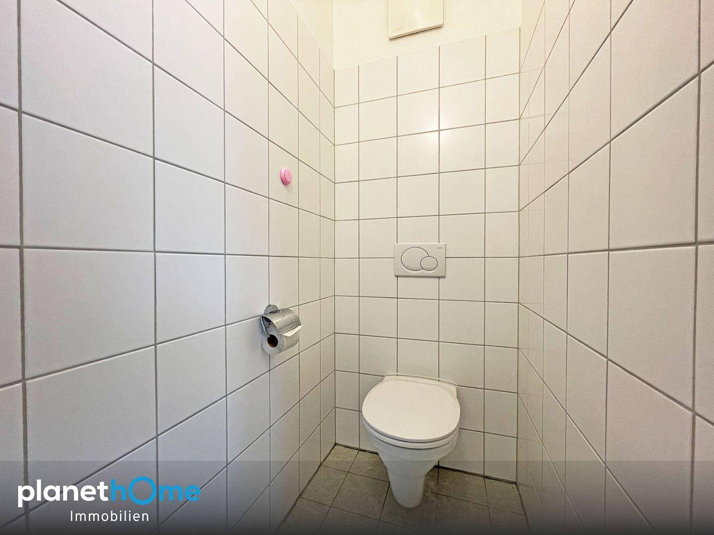 Kleines, vollständig gefliestes WC mit wandhängender Toilette und Spülkasten.