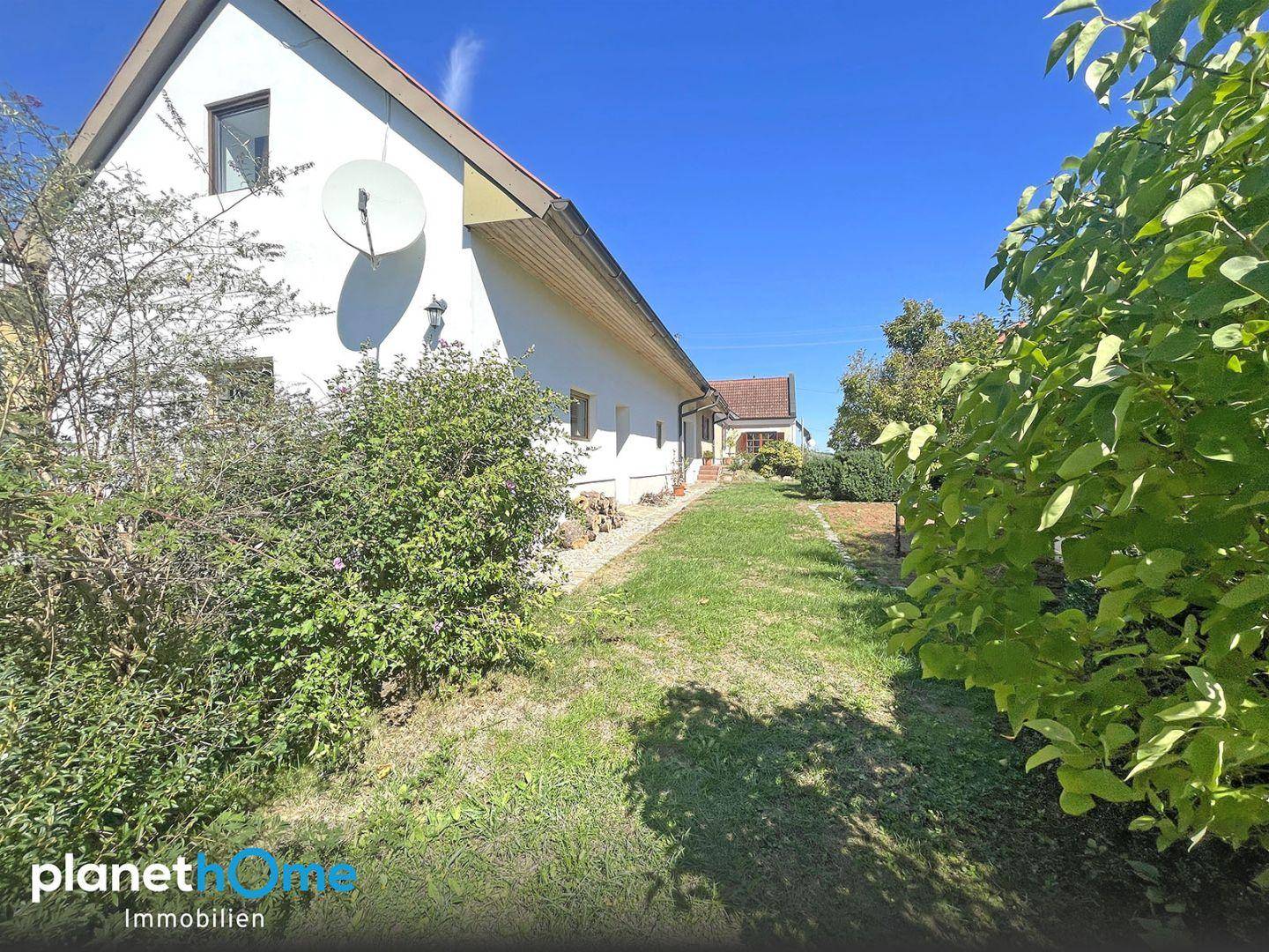 Vorderansicht des Hauses mit Garagentor, gepflegtem Gartenbereich und Dachfenstern unter blauem Himmel.