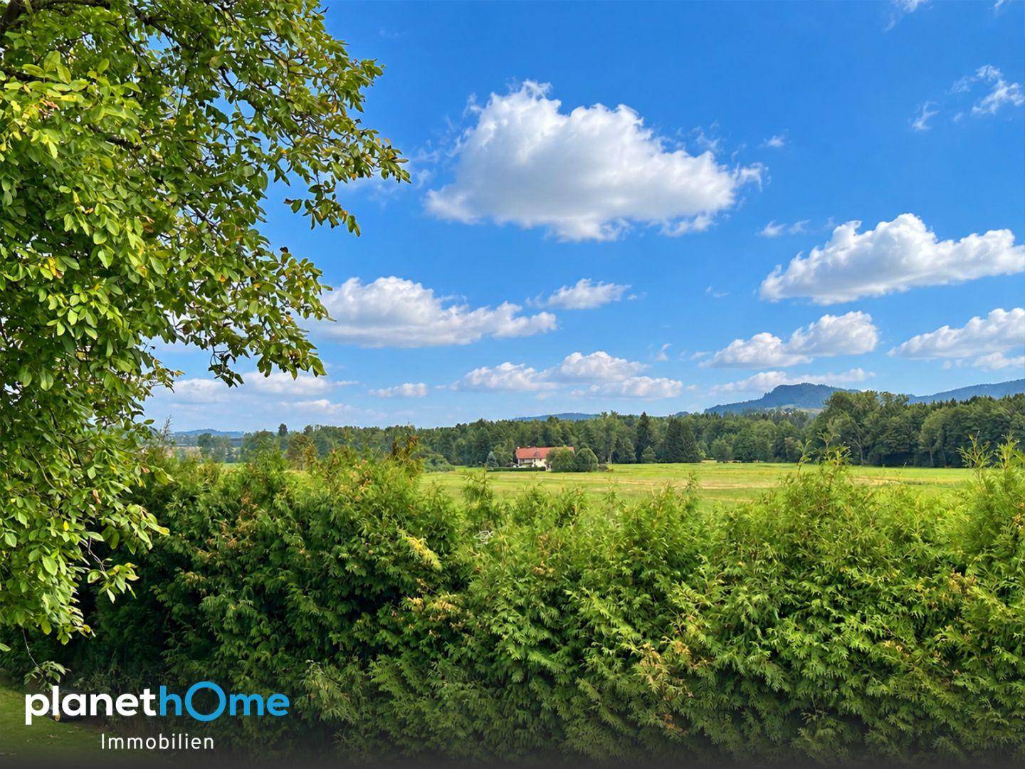 Malerischer Ausblick über weite Felder und Wälder mit einem Haus in der Ferne.