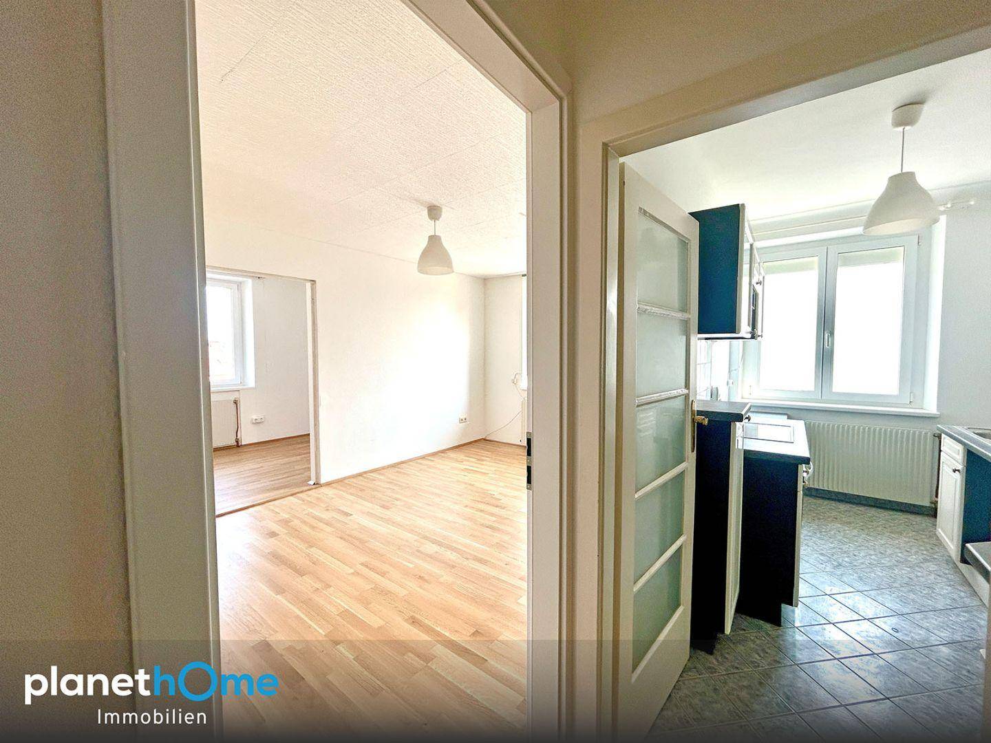 Blick vom Flur in ein leeres Zimmer und eine Küche mit Fenster.