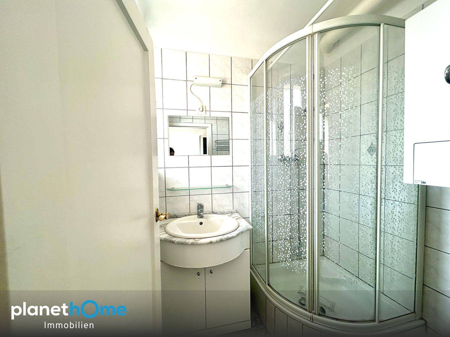 Badezimmer mit Eckdusche, Einzelwaschbecken und weißen Fliesen an den Wänden.