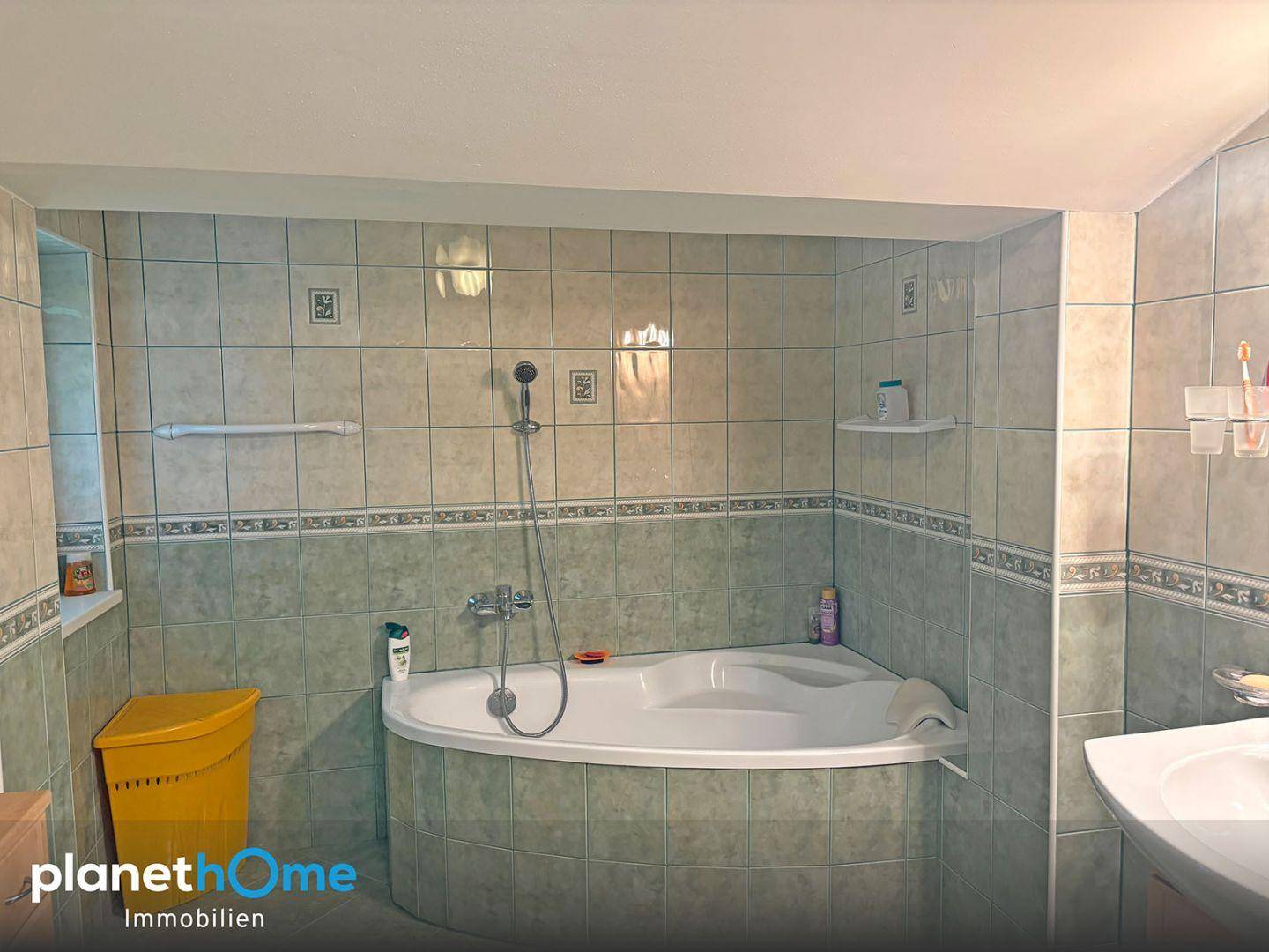 Badezimmer mit Eckbadewanne und hellgrünen Fliesen in traditionellem Design.