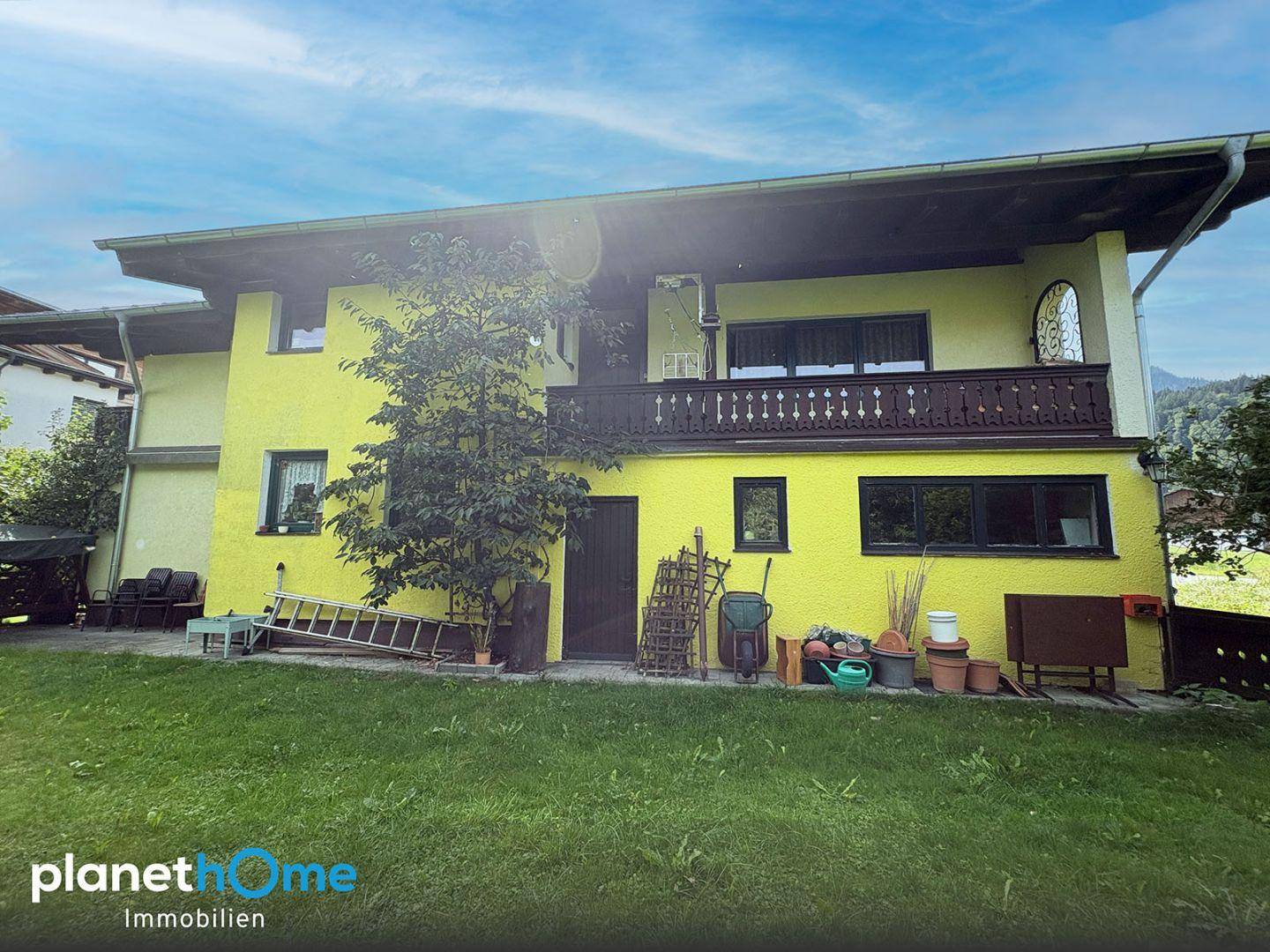 Rückseite des Hauses mit Garten, Balkon und verschiedenen Gartenutensilien.