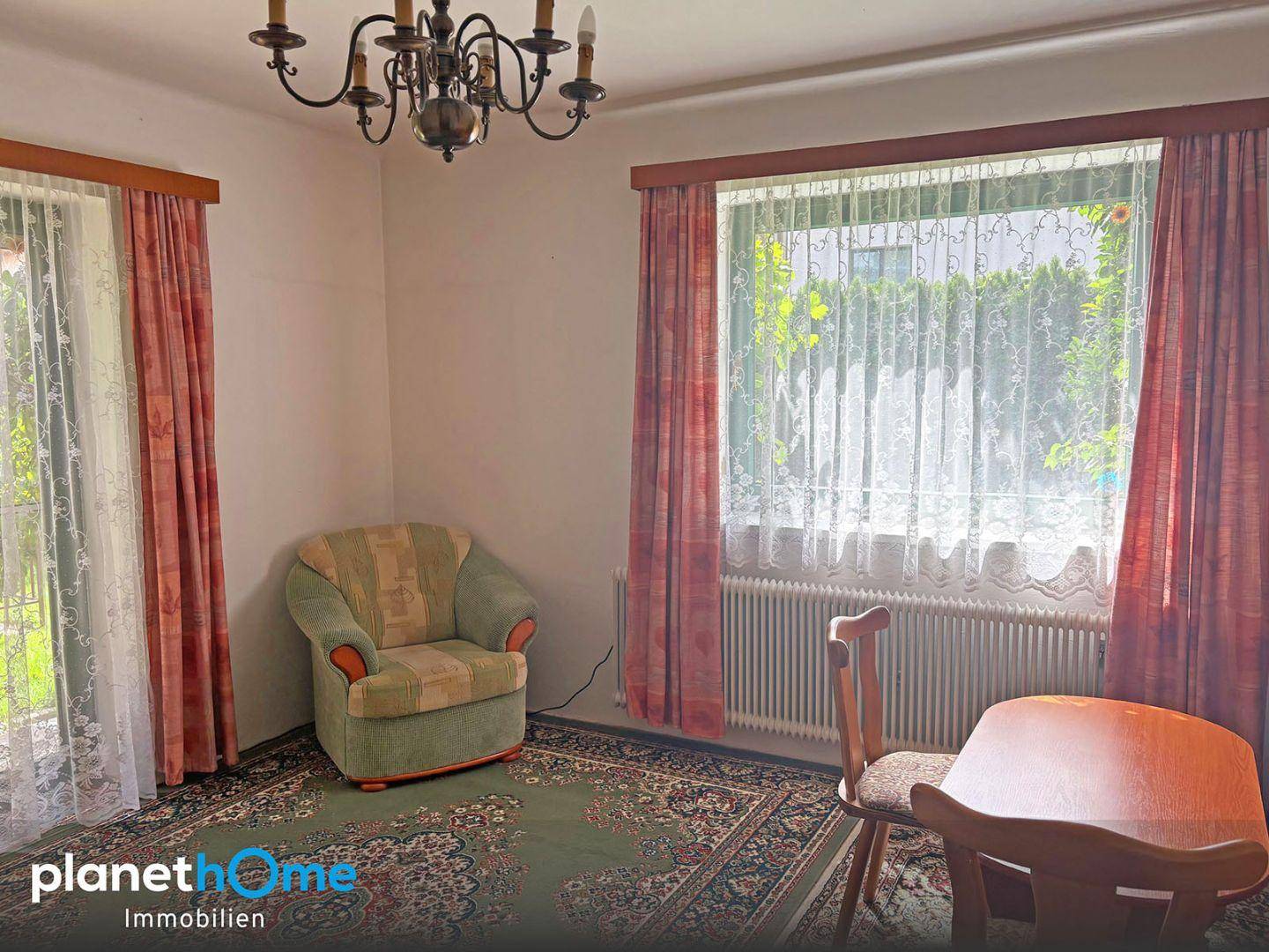 Wohnbereich mit Teppichboden, großem Fenster und traditionellen Vorhängen.