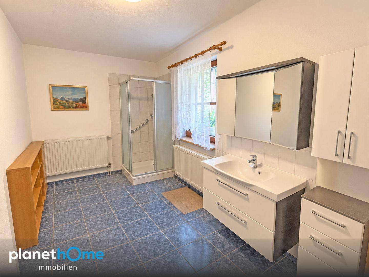 Badezimmer mit blauen Bodenfliesen, Duschkabine, modernem Waschtisch und einem Fenster.