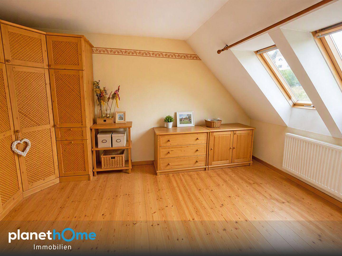 Geräumiges Zimmer im Dachgeschoss mit Holzboden, Holzmöbeln und zwei Dachfenstern.