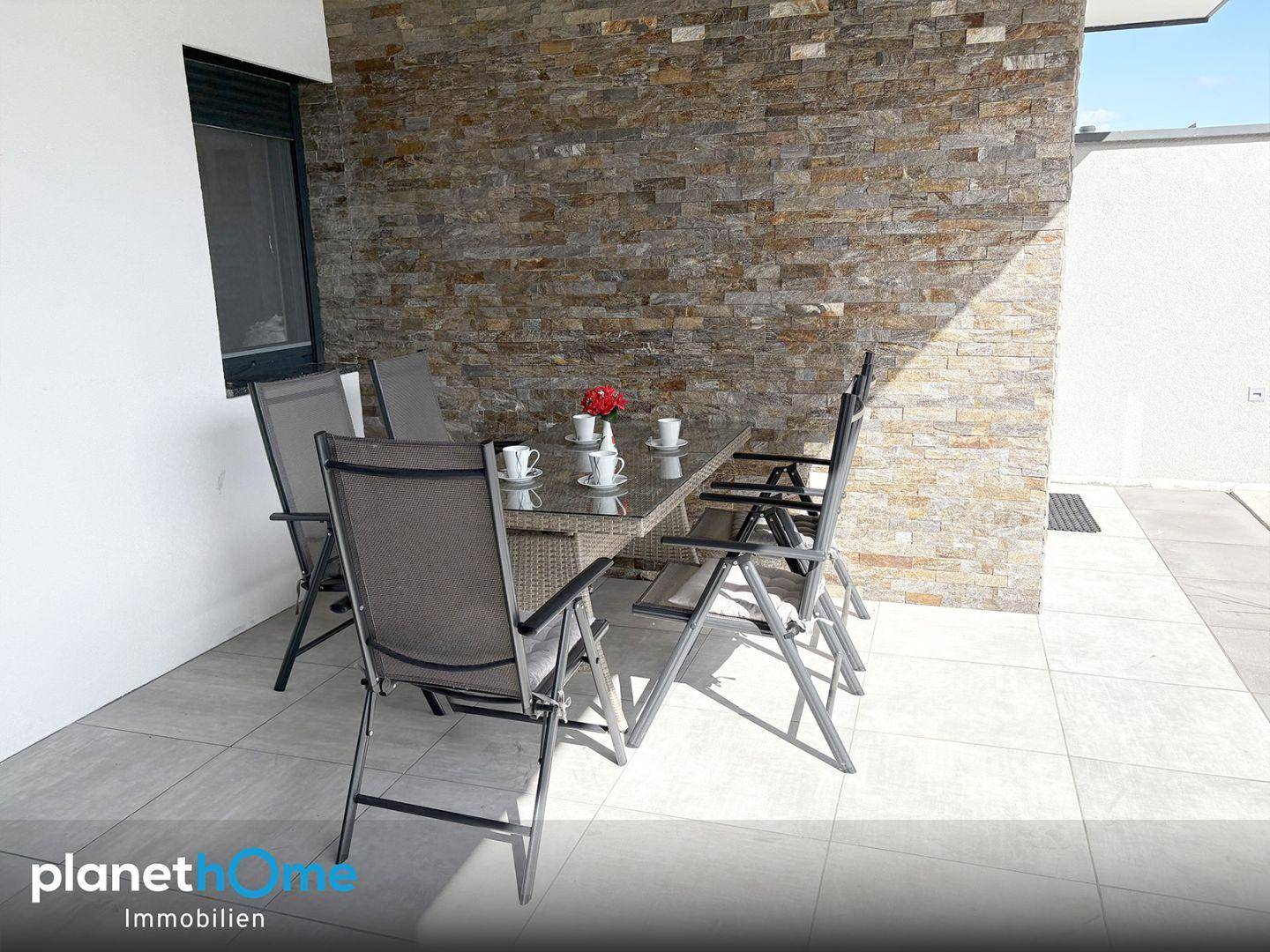 Überdachte Terrasse mit Esstisch und Stühlen, umgeben von einer dekorativen Steinwand.